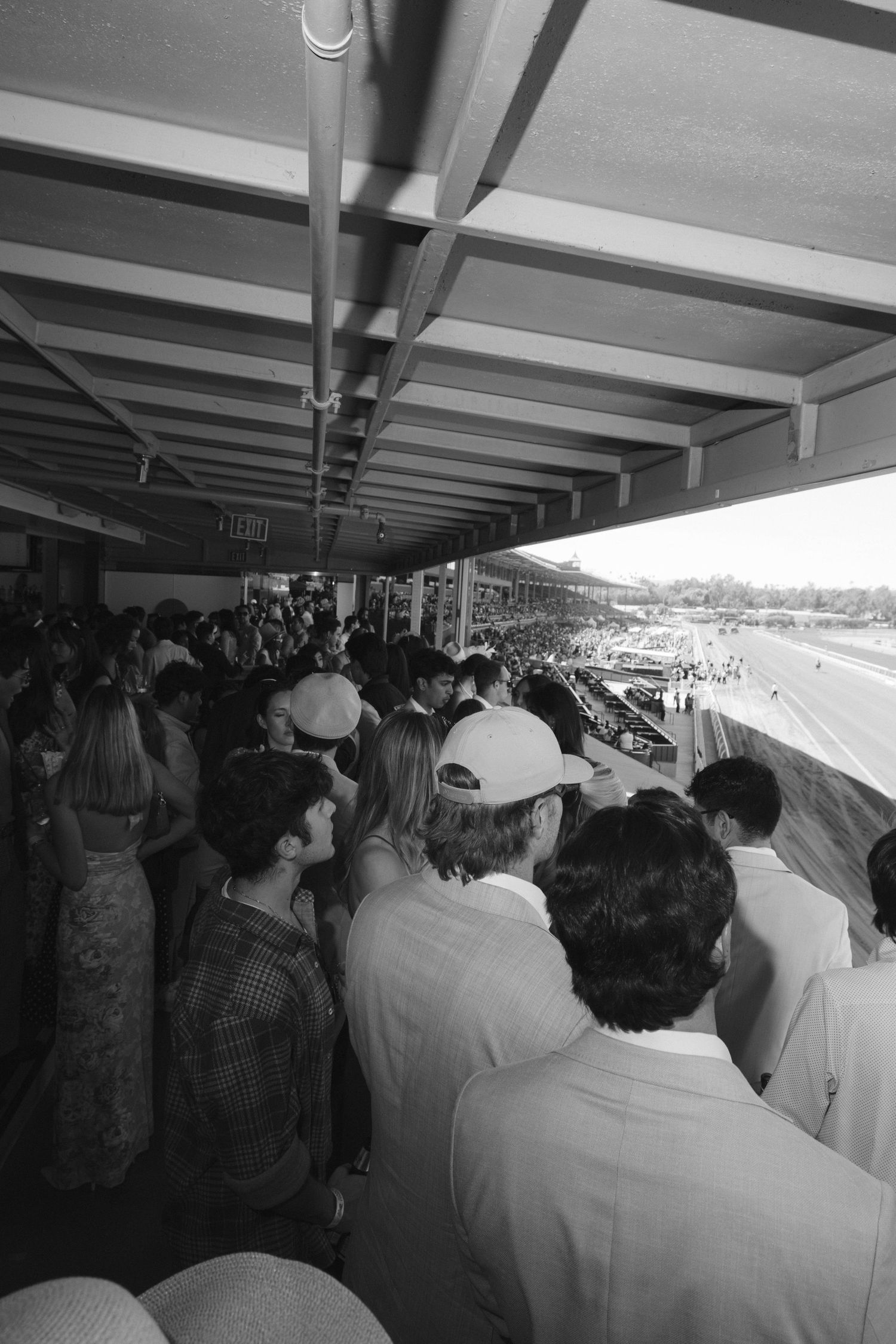 A black and white panoramic view of spectators watching from a covered stadium viewing area.