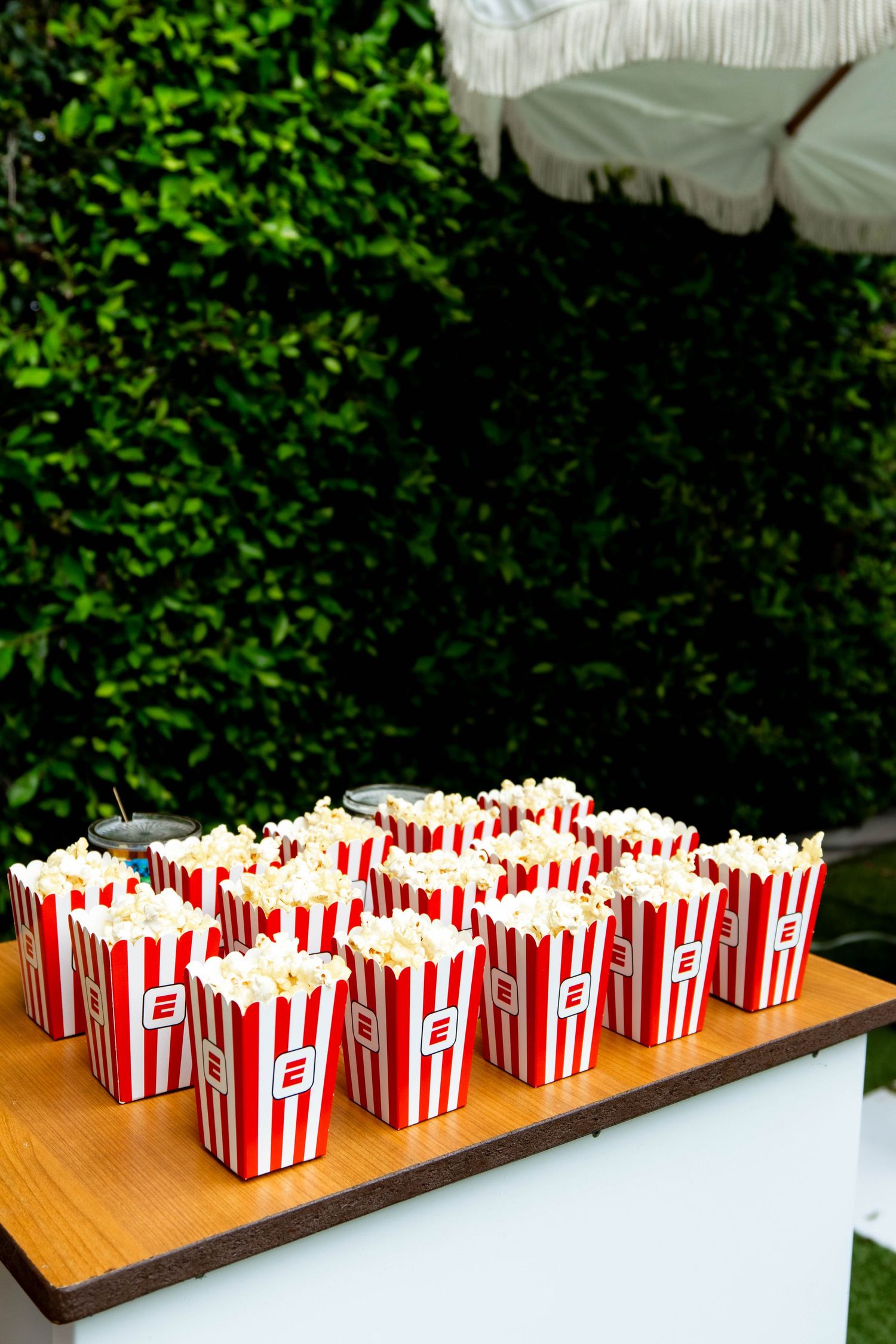 Classic red and white striped popcorn containers arranged on a wooden table with greenery in background.