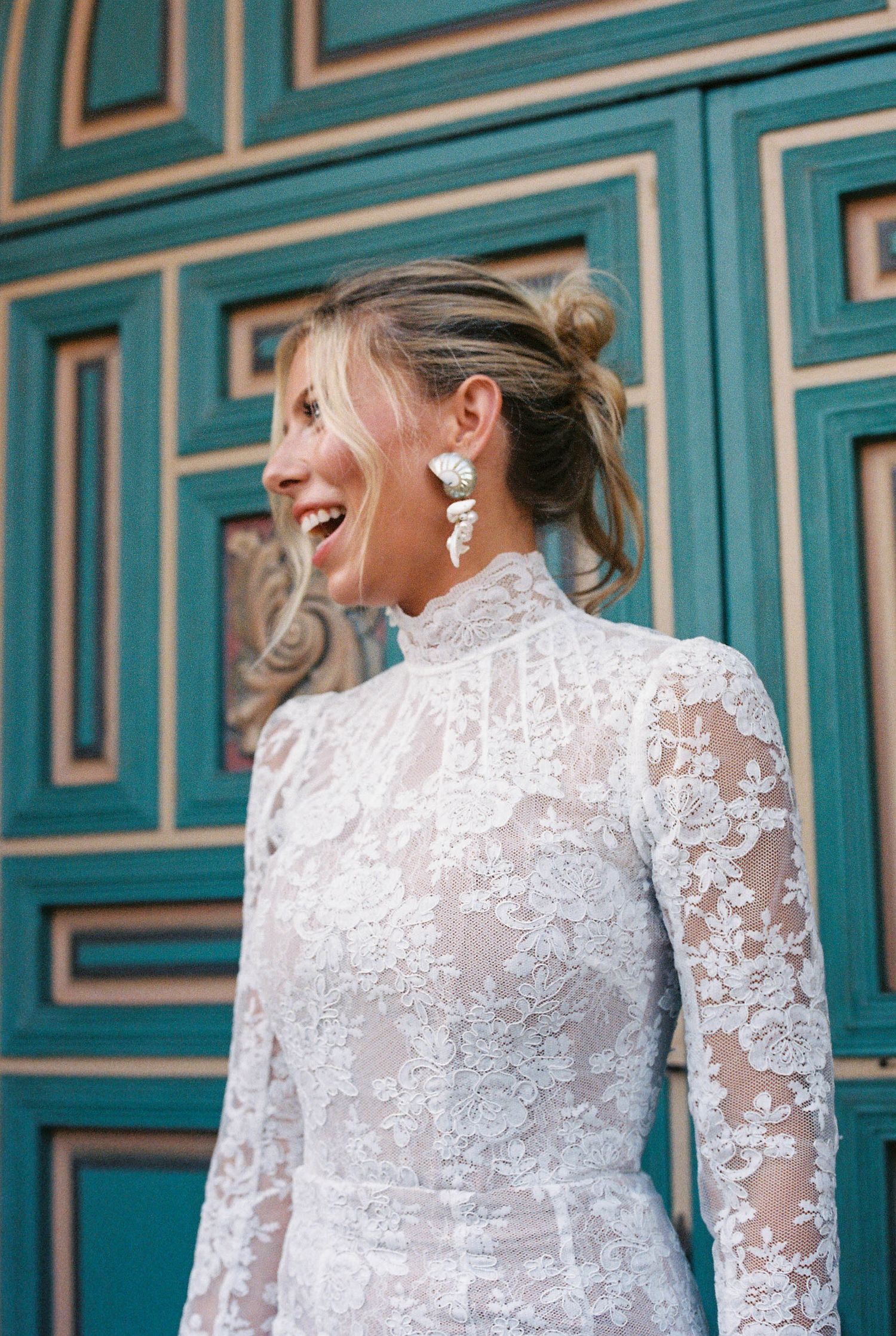 People wearing elegant white lace attire standing against a turquoise paneled wall.