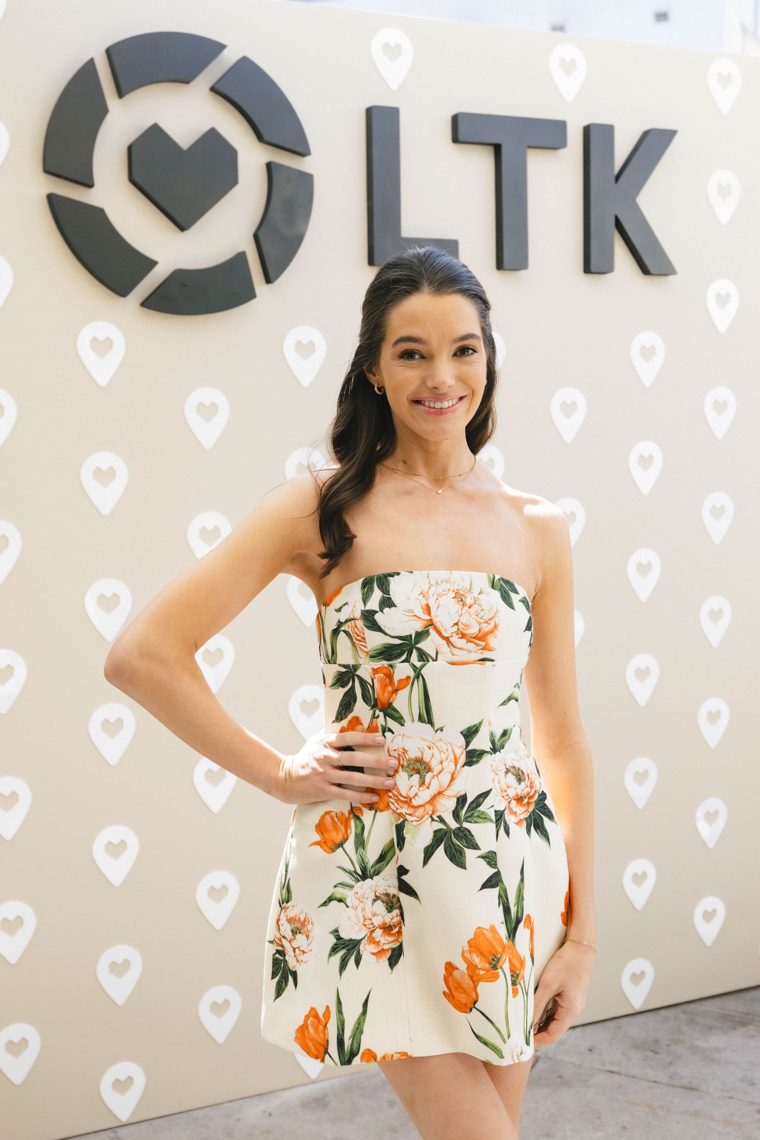 Floral summer dress with orange and green tropical print against white heart patterned background.