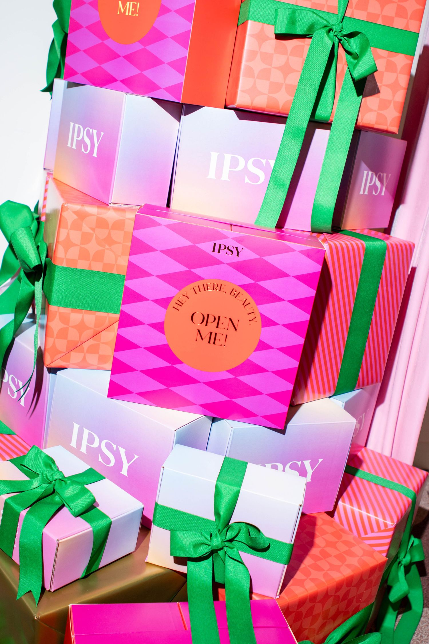 Collection of Ipsy beauty boxes with pink geometric patterns and green ribbon decorations.