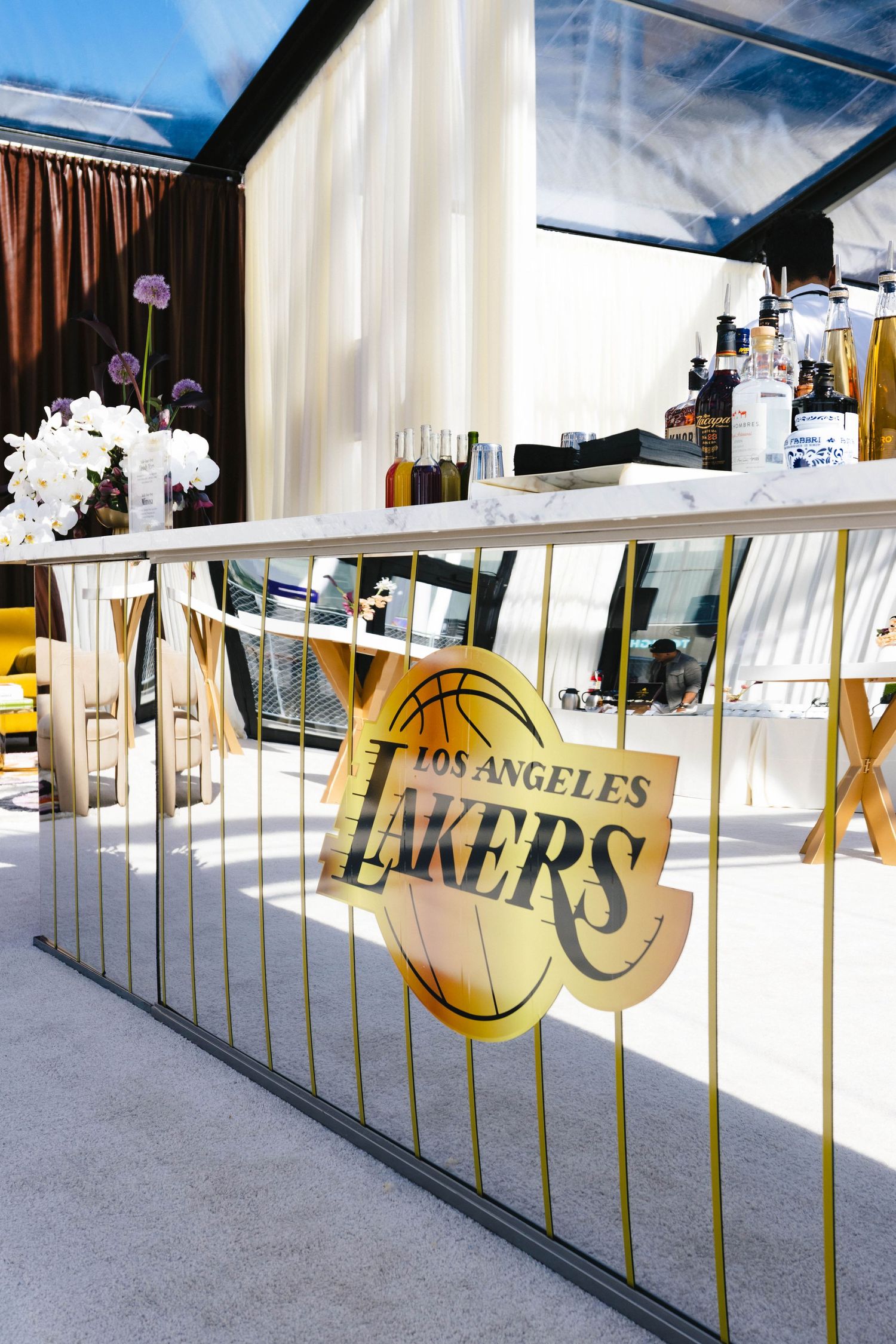 Los Angeles Lakers branded gold railing at an elegant event bar setup with white flowers and bottles.