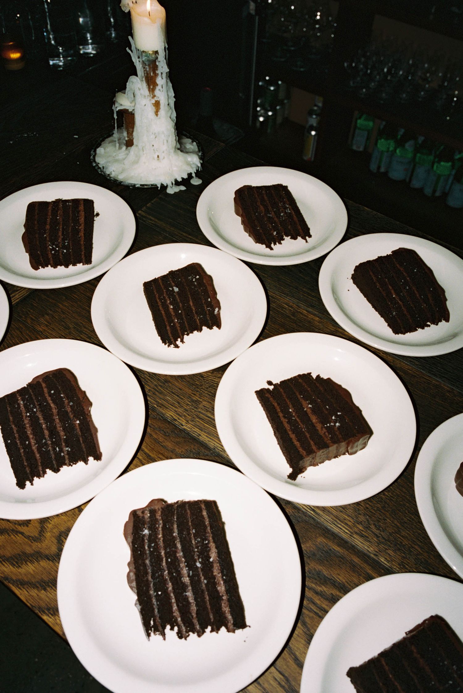 Multiple slices of chocolate cake arranged on white plates in a dimly lit setting.