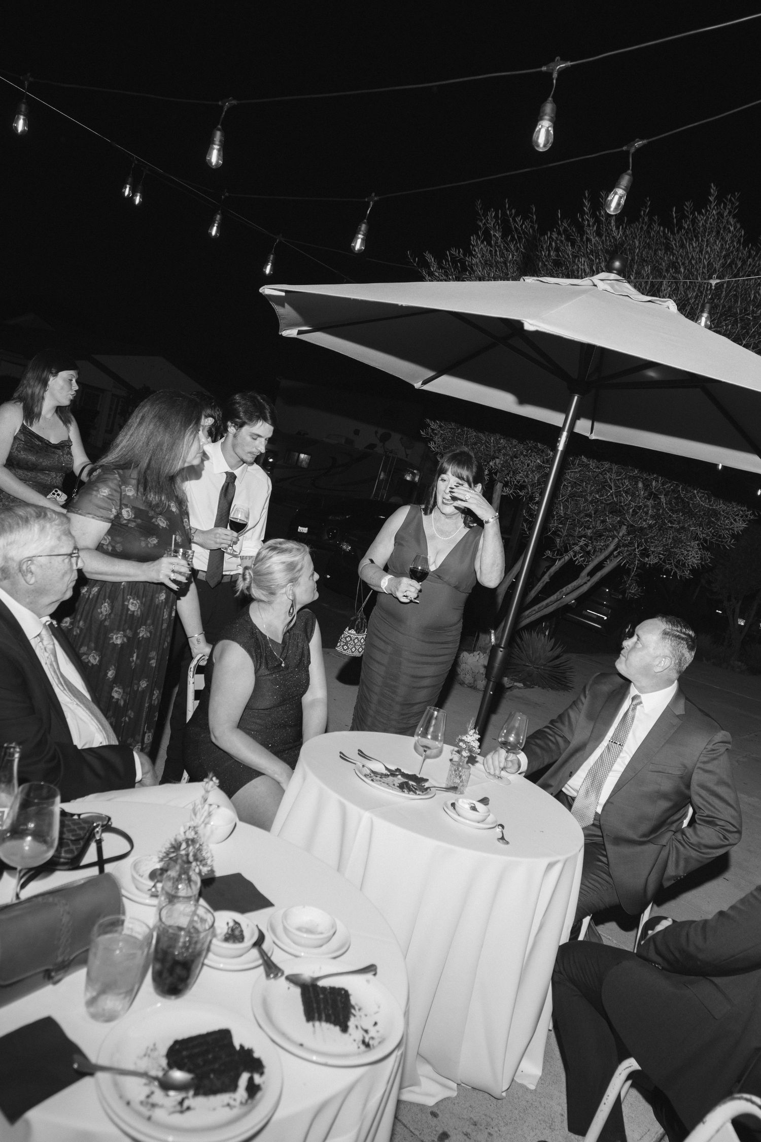 People dining at elegant white-clothed tables under string lights at an outdoor event.