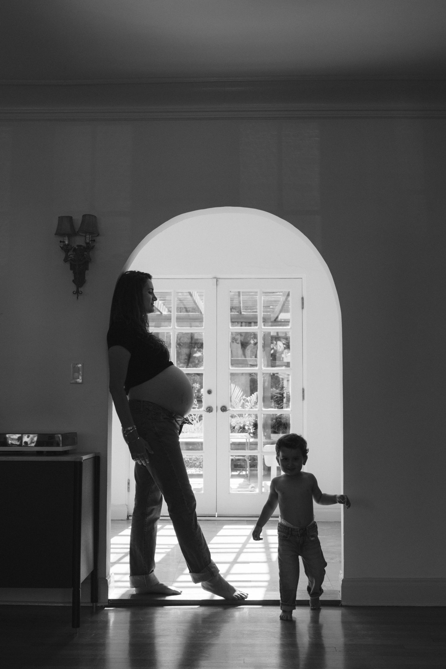 Silhouette of pregnant woman and small child standing in doorway with arched window.