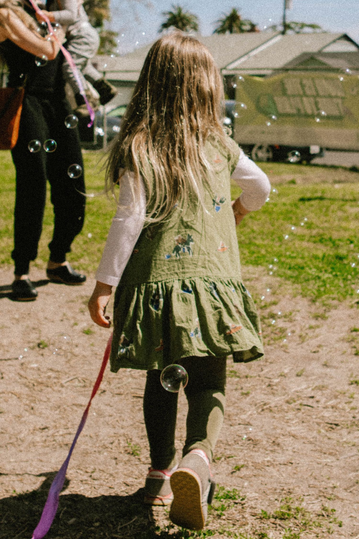 Child walking on a dirt path wearing a green dress and holding a purple wand.