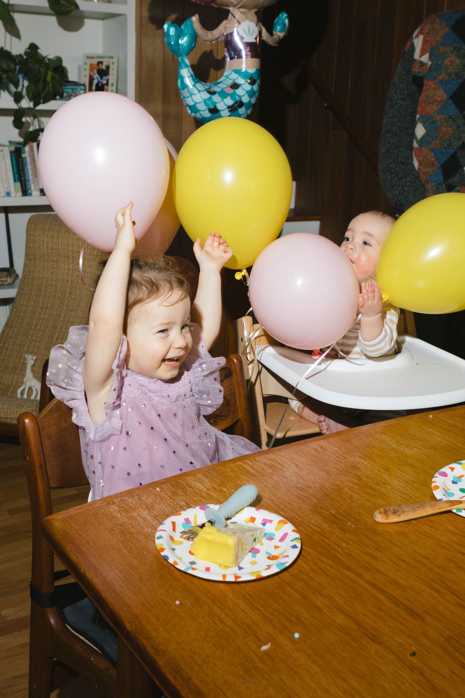 Children celebrating with pink and yellow balloons at a party with decorated plates.