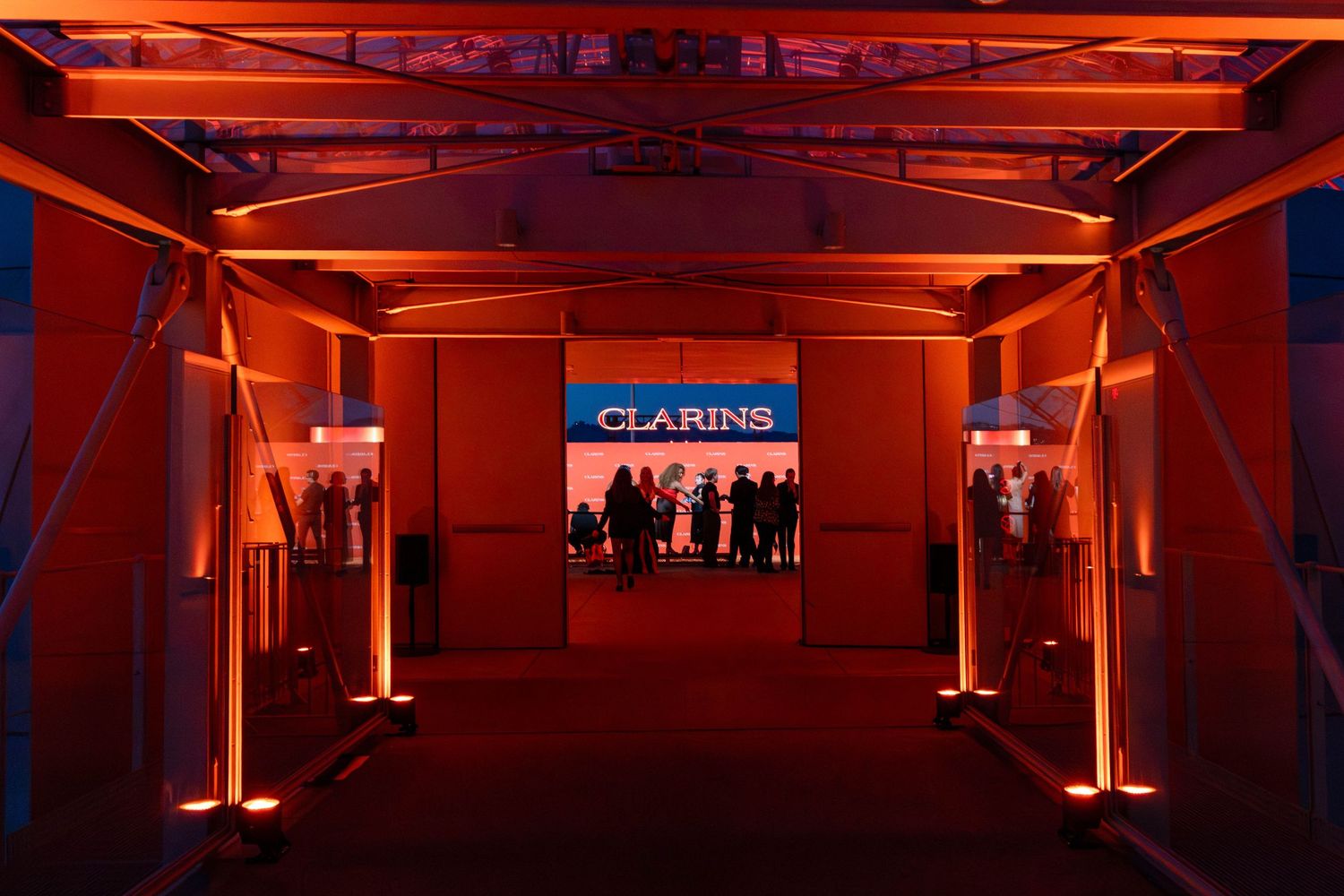 Clarins branded event entrance with dramatic red-orange lighting illuminating a tunnel walkway leading to a glowing display.
