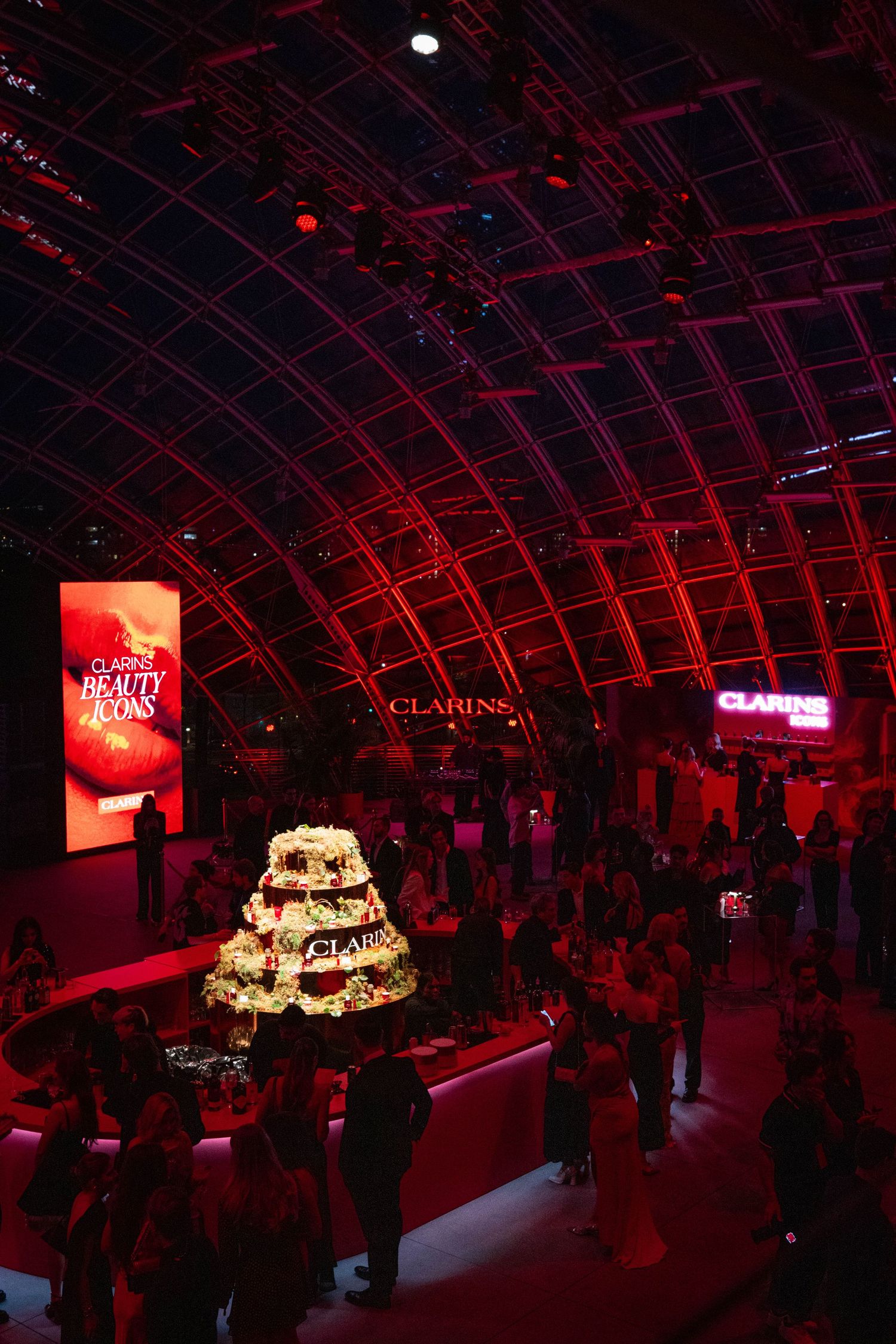 Elegant event space with red lighting and tiered display at a Clarins beauty brand launch party.