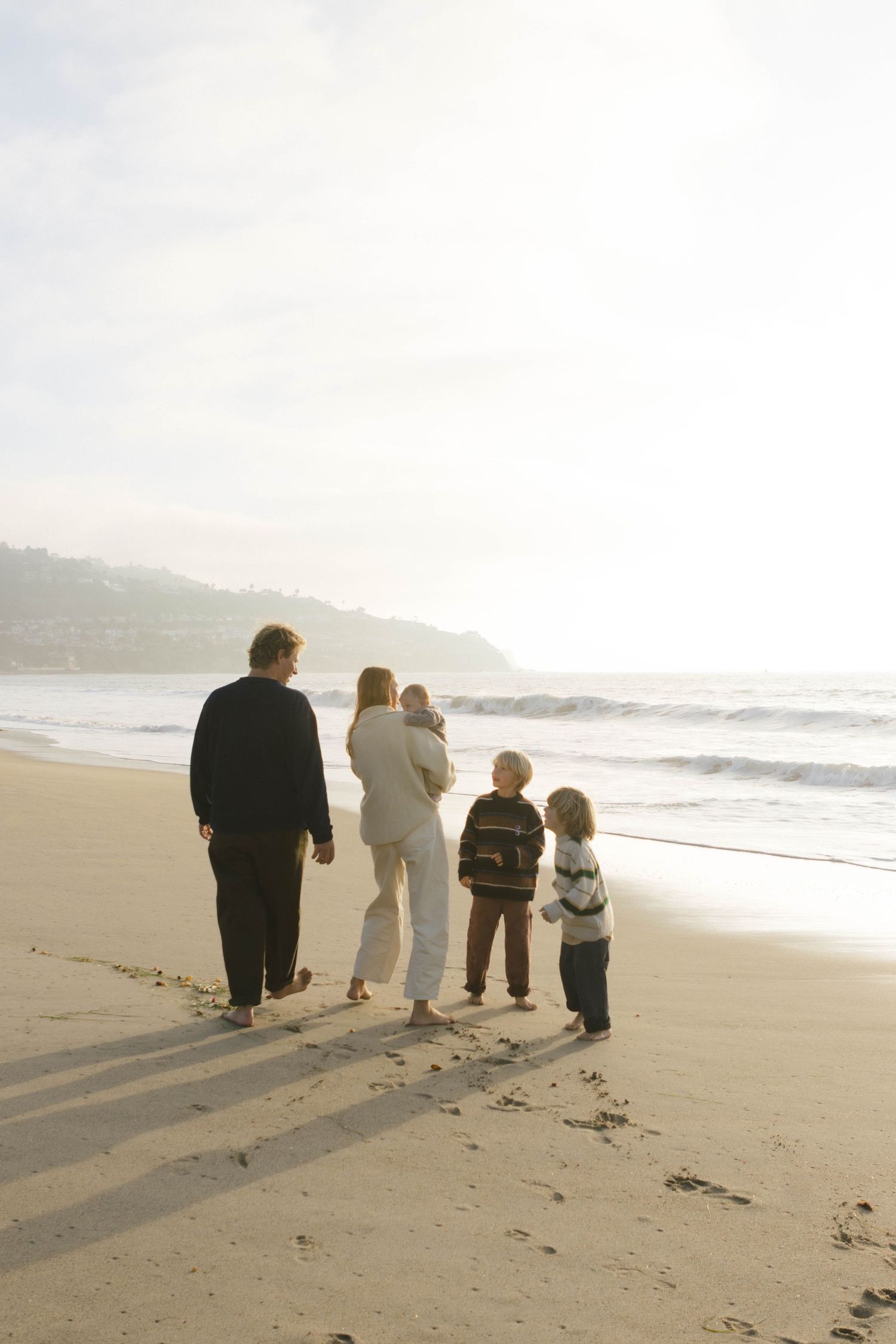 A group of people walking together along a misty beach shoreline at sunset.