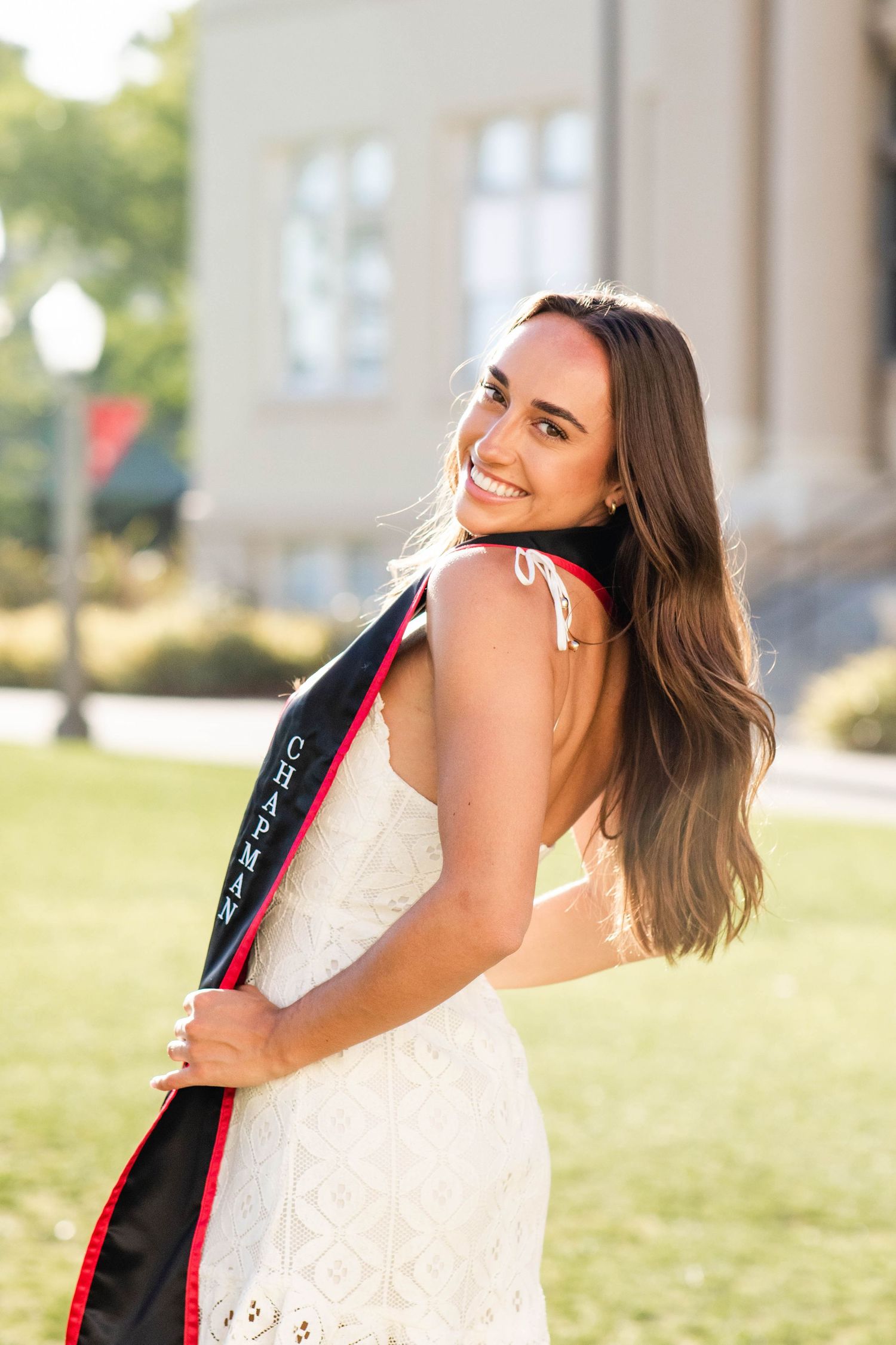 Graduate in white dress and graduation stole posing outdoors.