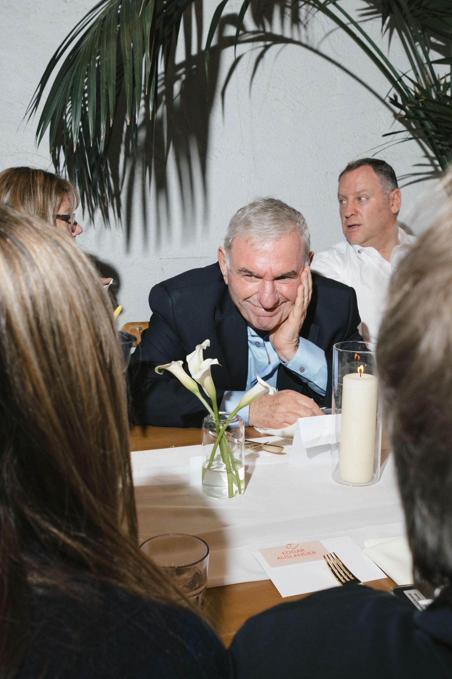 A group of people gathered around a dining table with a white lily flower centerpiece and candlelight.