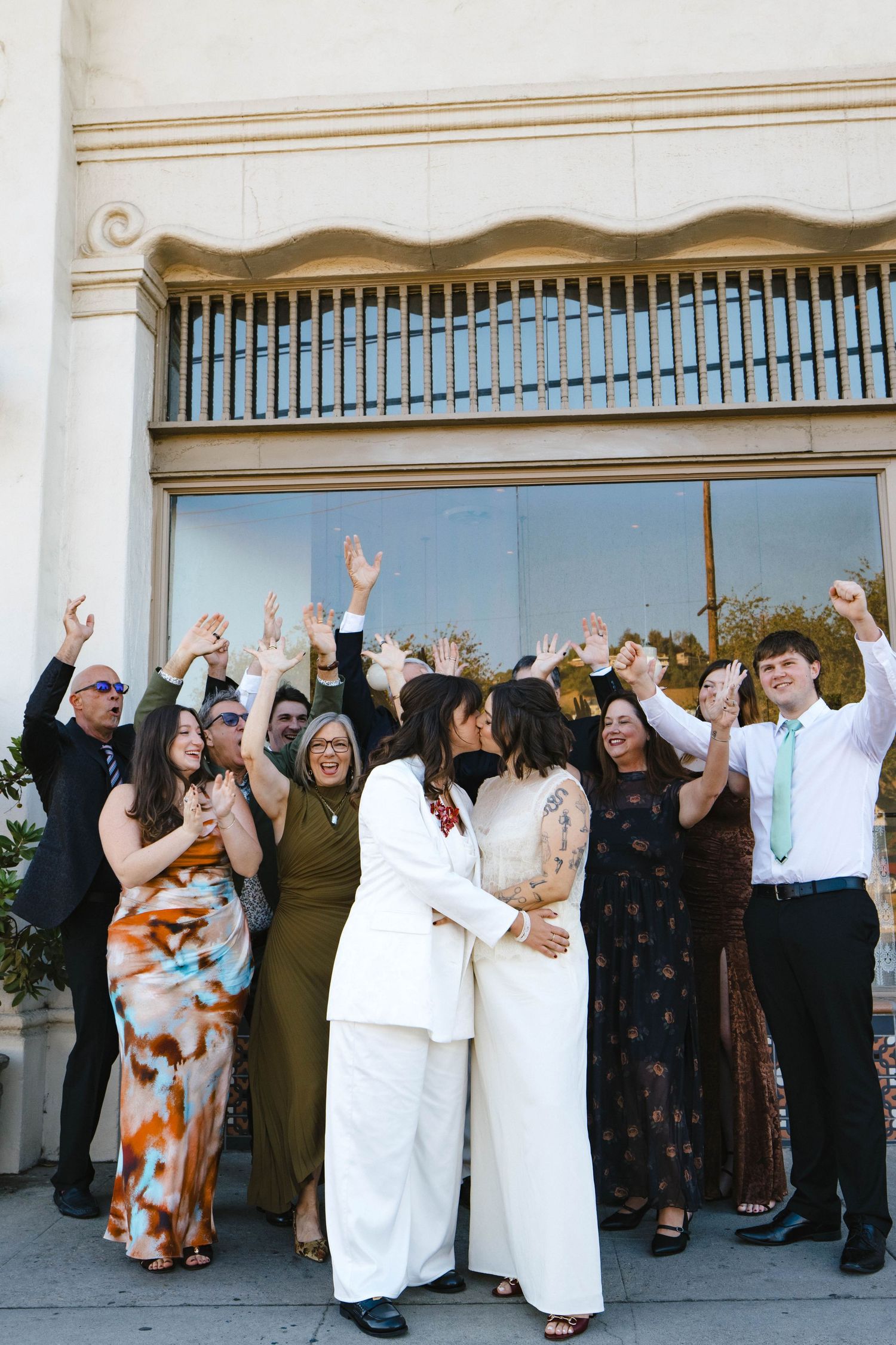 Large group of wedding guests raising their hands in celebration outside a building.