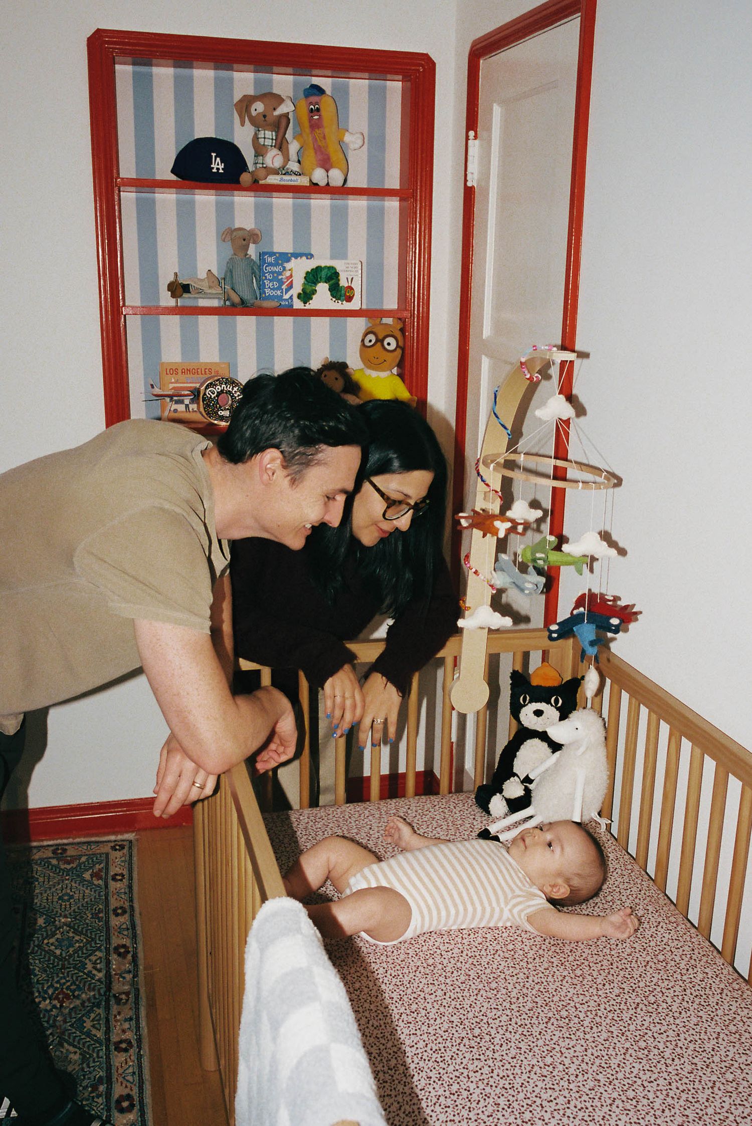 A nursery scene with stuffed animals on shelves and a crib with striped wallpaper.