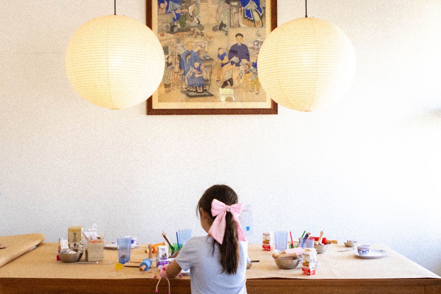 Person sitting at a table under pendant lights with crafting supplies spread out.