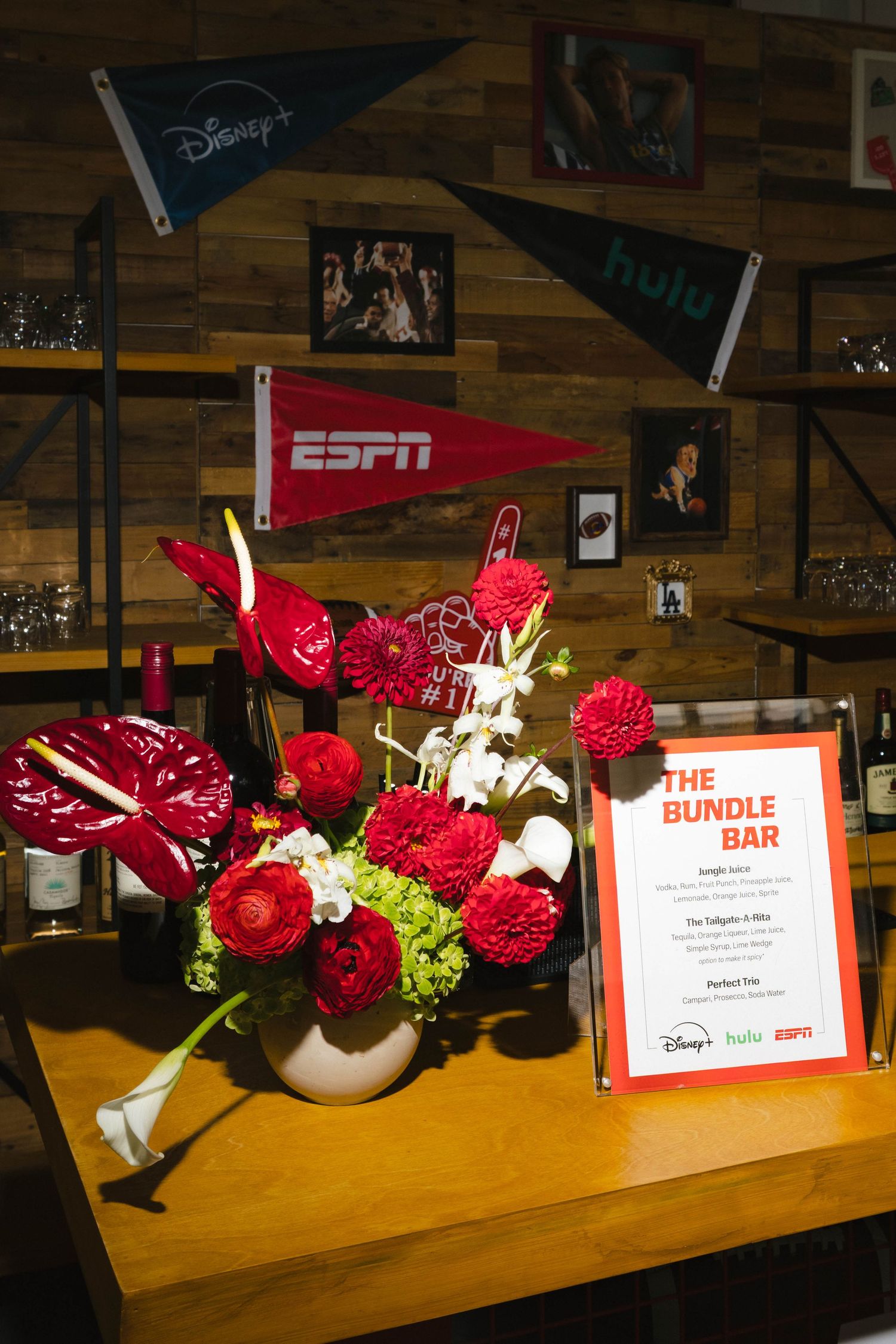 Sports-themed display with ESPN pennant, Disney flags, and red floral arrangement on wooden table.