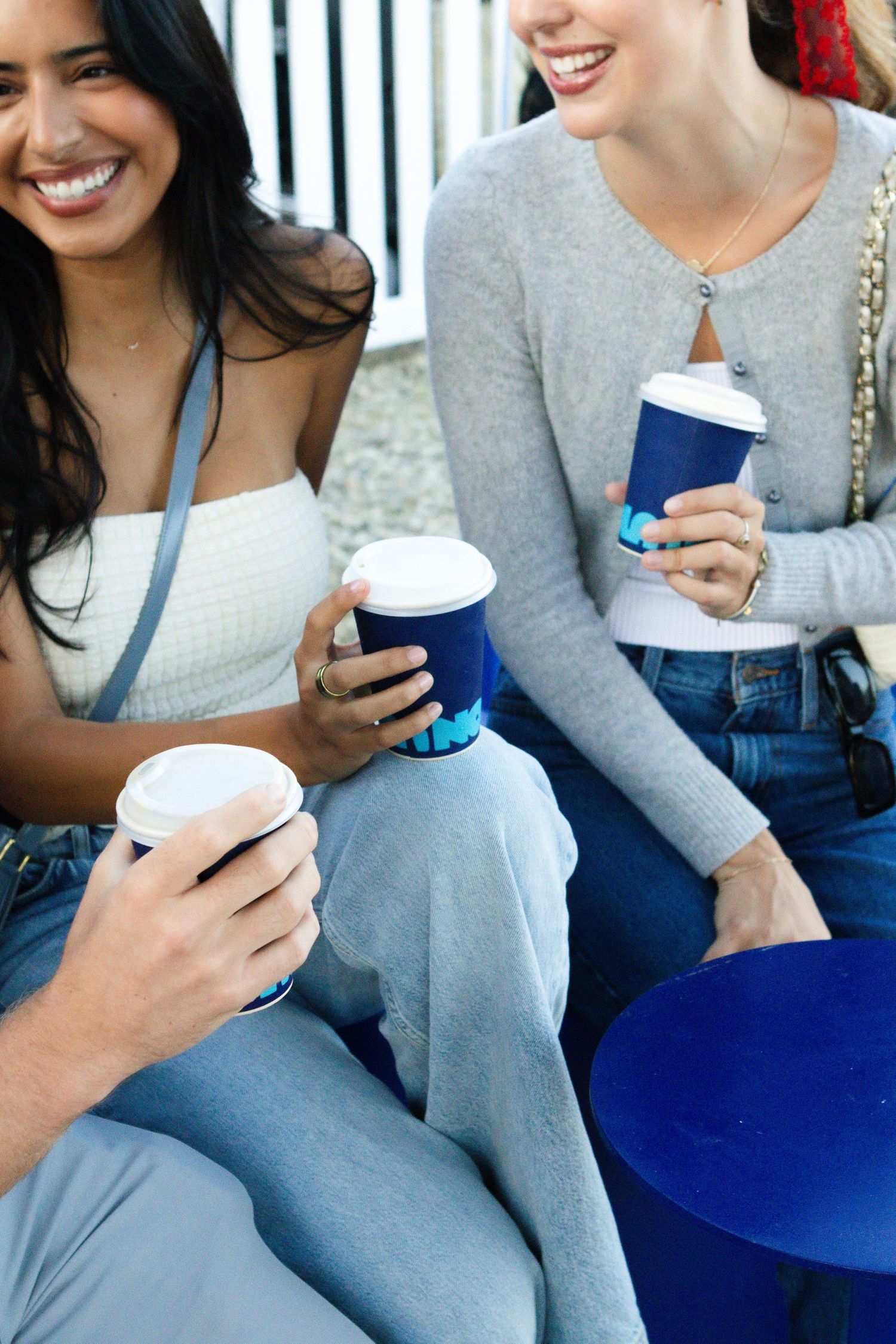 People sitting together holding blue coffee cups and wearing casual attire.