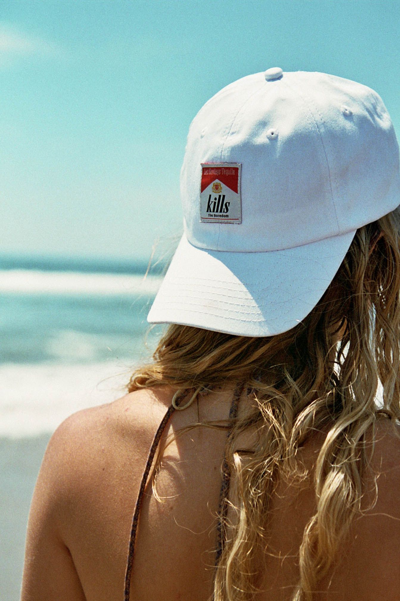 A white baseball cap with a logo photographed against an ocean backdrop.