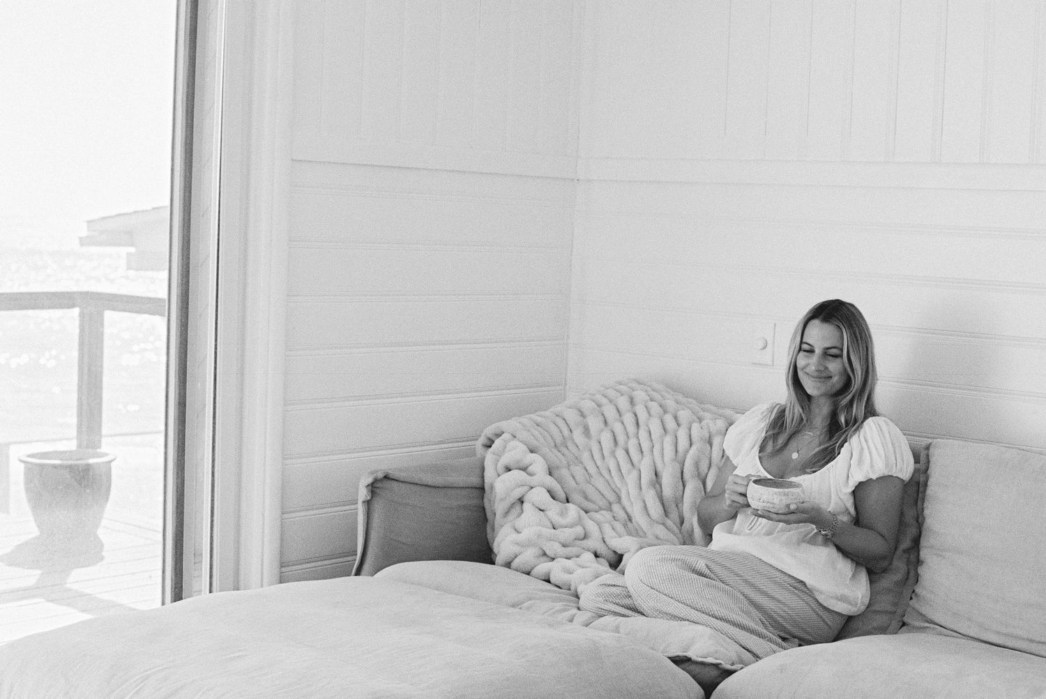 Two people relaxing on a white couch in a bright, sunlit living room interior.