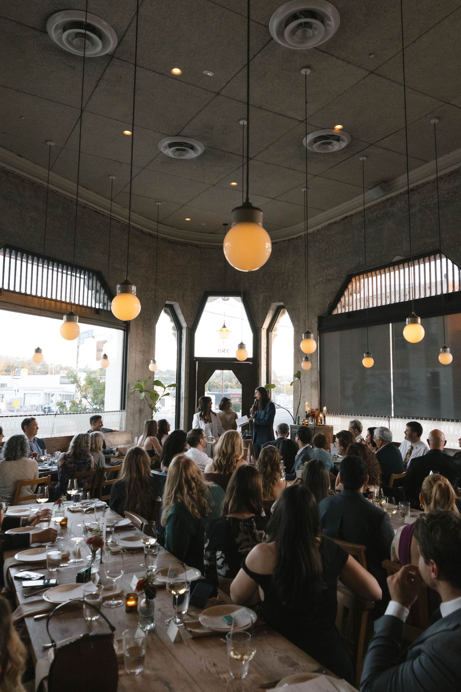 A crowded restaurant interior with round pendant lights and diners seated at tables during a busy dinner service.