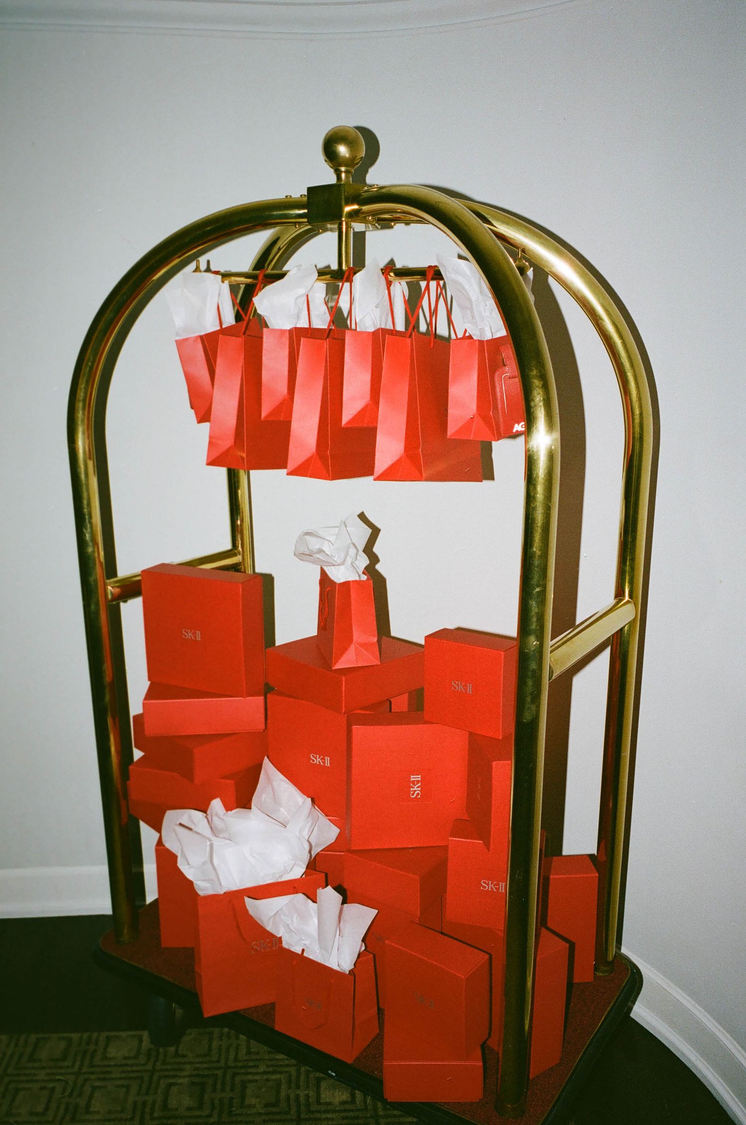 Hotel luggage cart stacked with red shopping bags and boxes in a hallway.