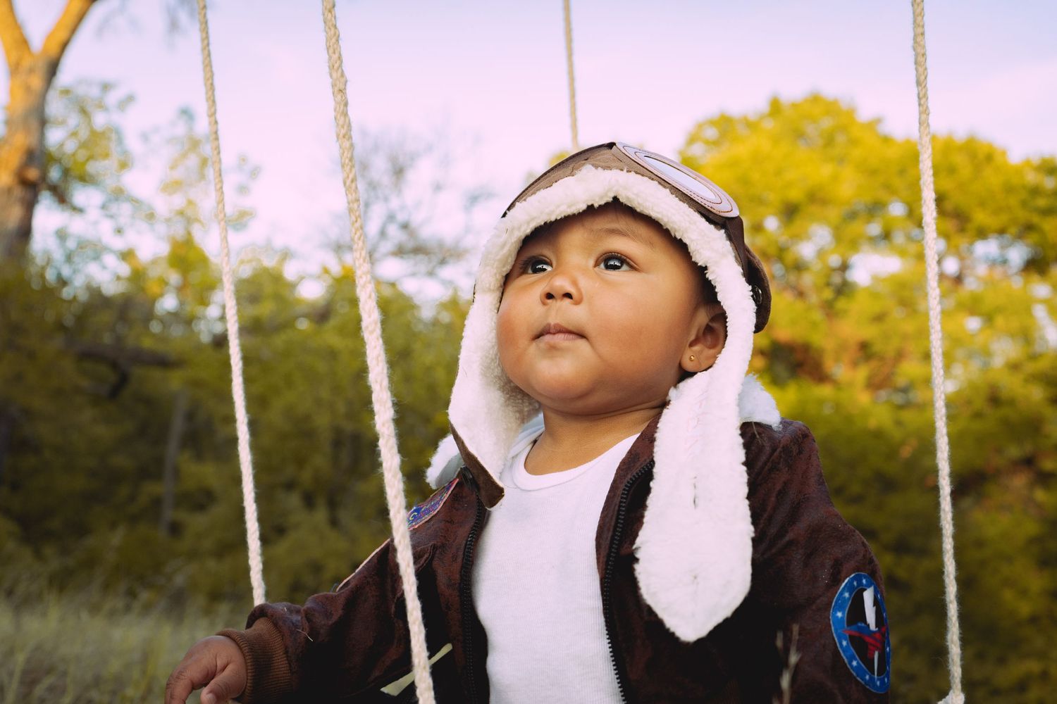 A person wearing a white beanie and blue backpack stands against a backdrop of autumn trees and poles.