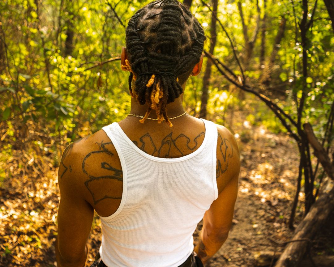 Person in white tank top poses against sunlit autumn forest backdrop.