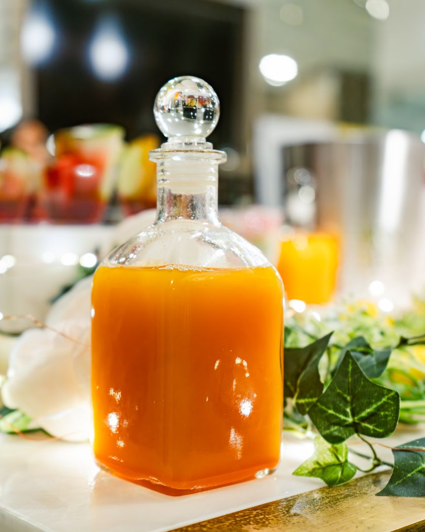 Orange-colored liquid in glass decanters displayed with fresh greenery and ambient lighting.