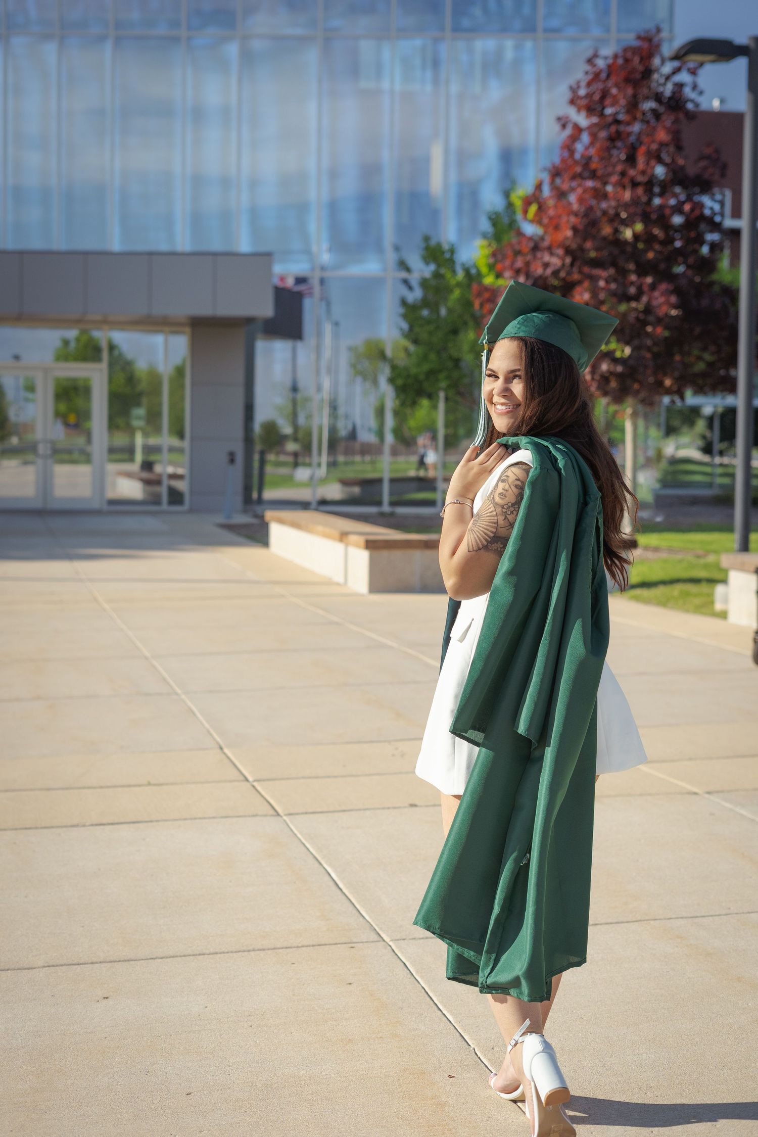 Green graduation gown and cap twirling in front of modern building.