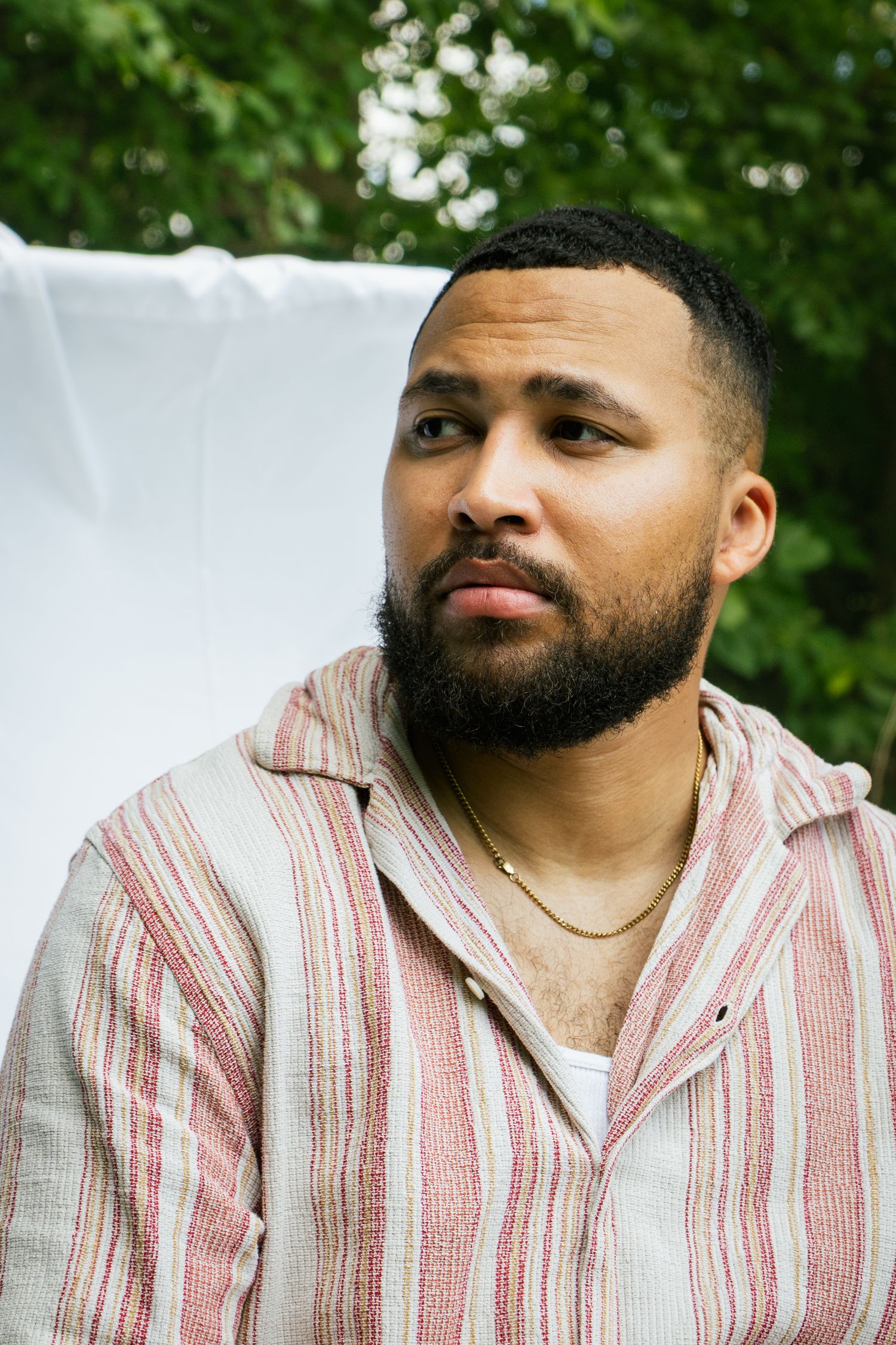 Side profile portrait of a person in striped shirt against white backdrop with natural lighting.
