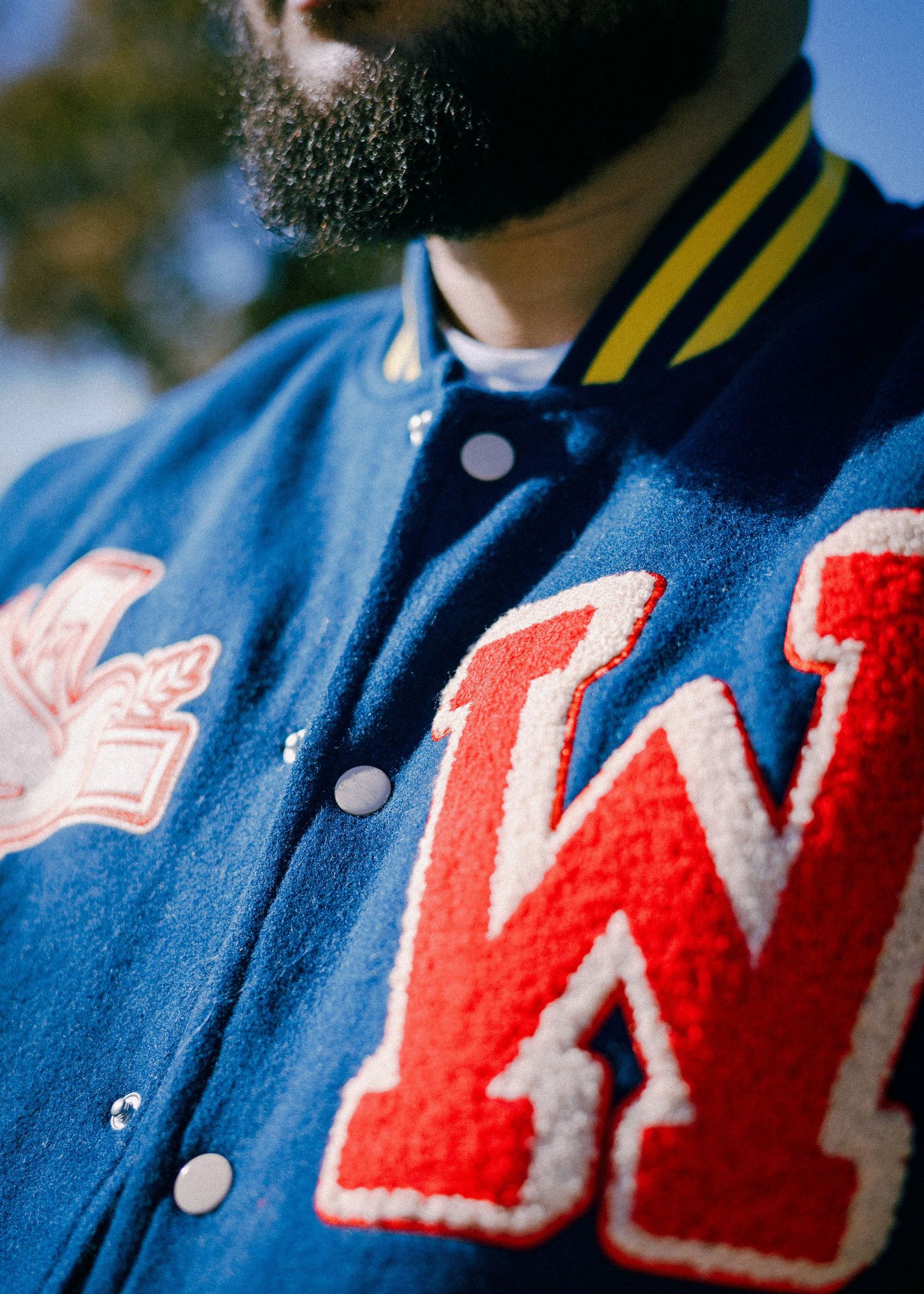 Close-up view of a blue varsity jacket with red chenille letters spelling 'WI' in a retro collegiate style.