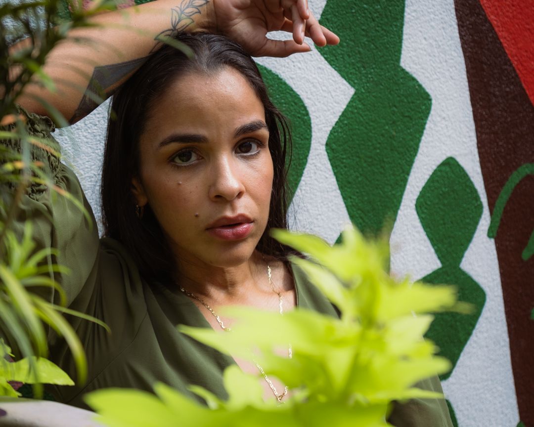 A person poses outdoors against a green and white background with tropical foliage in the foreground.