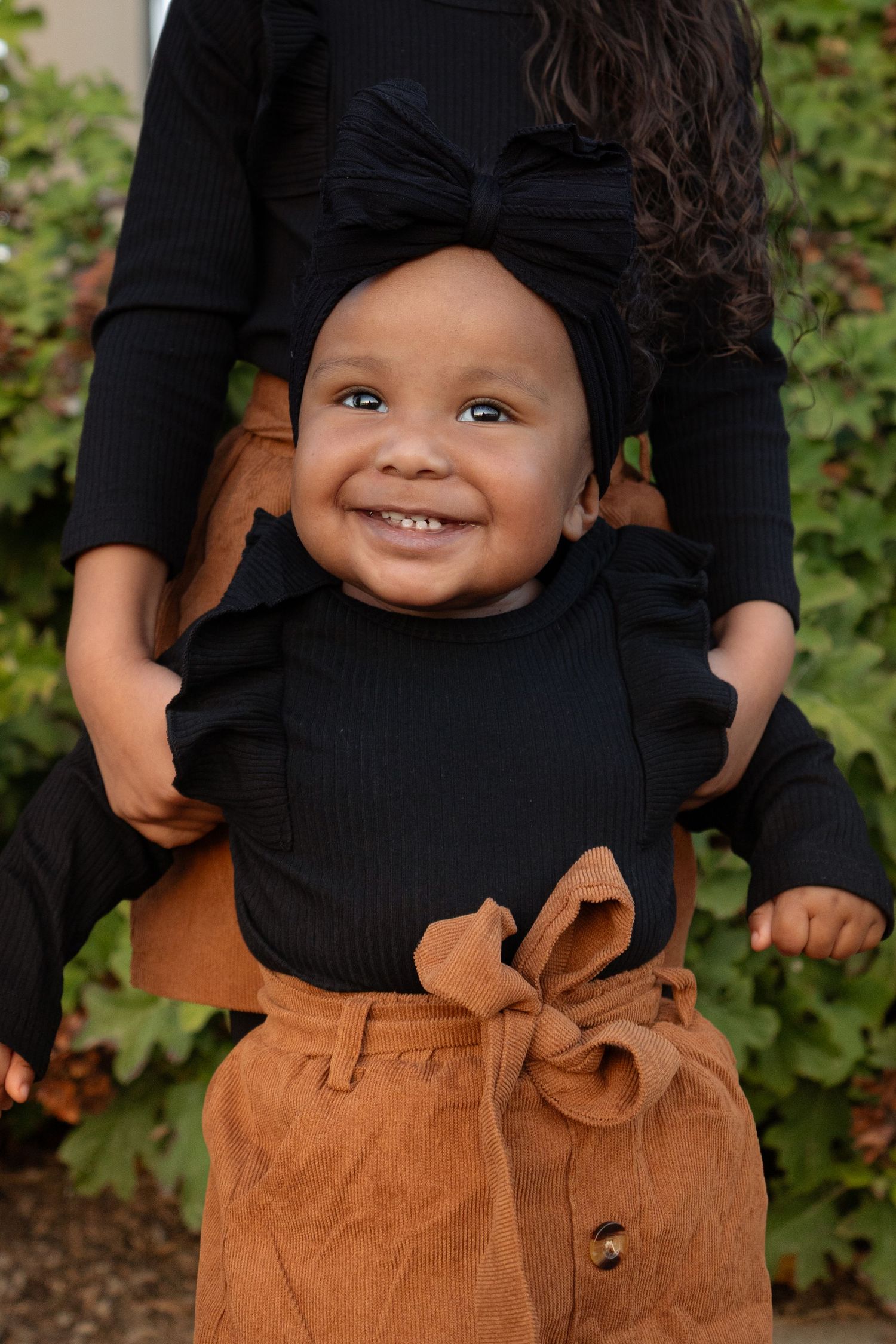 Close-up portraits showing a black top and brown pants against green foliage.