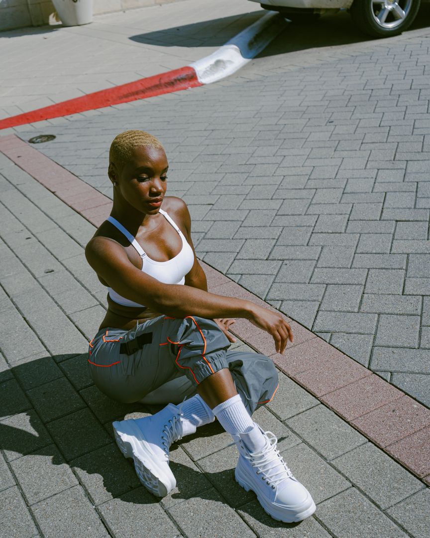 Person in athletic wear sits on urban pavement for editorial photoshoot during a sunny day.