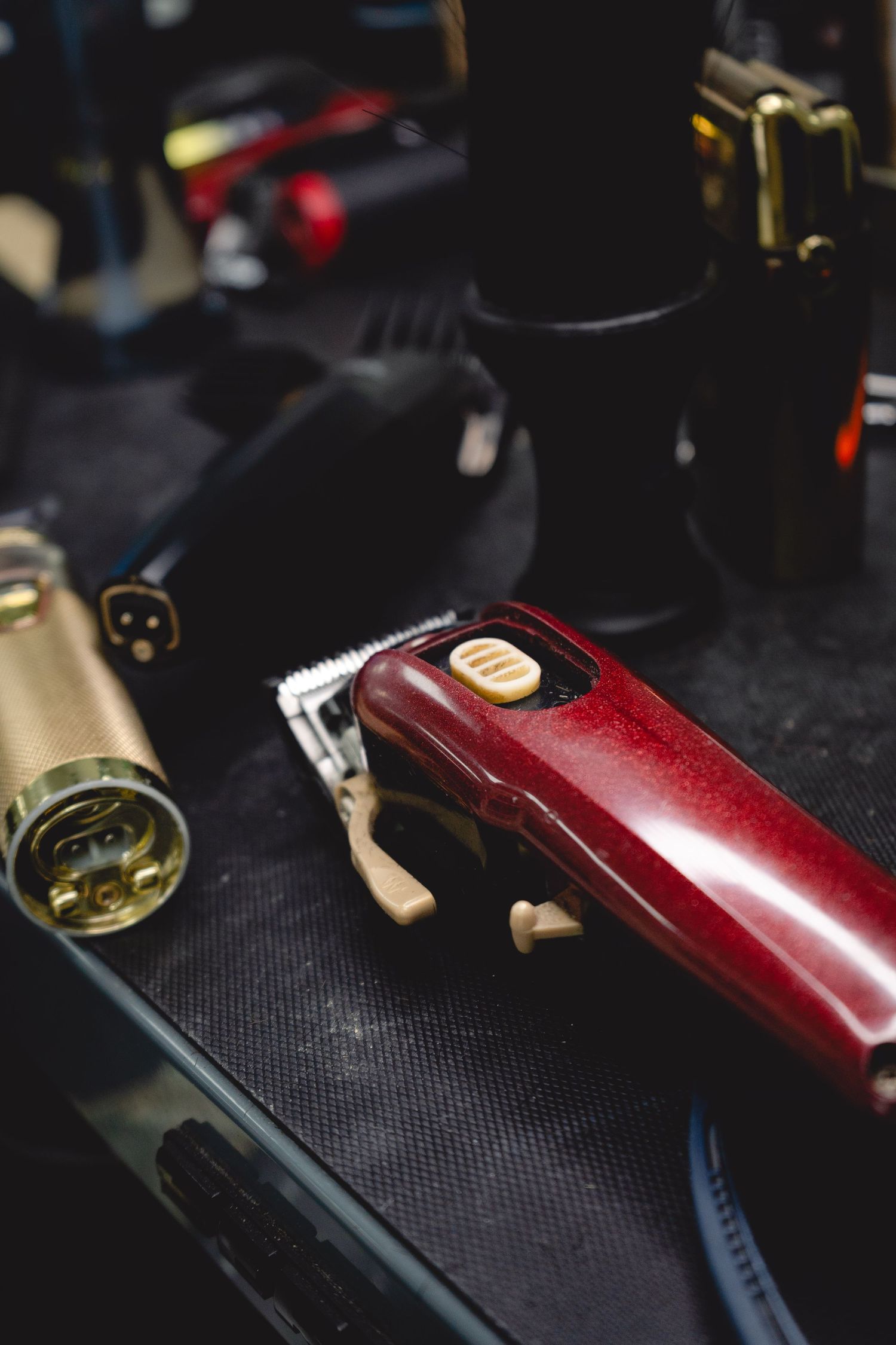 Close-up detail of red and black professional hair clippers on textured surface.