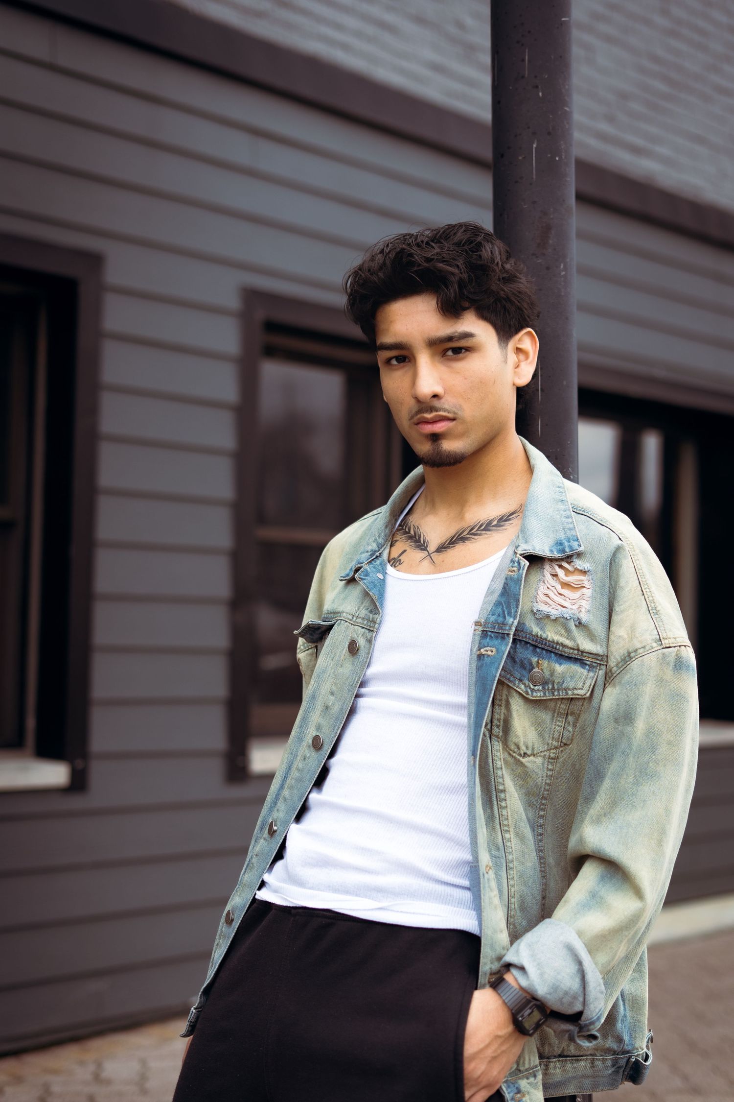 Model wearing white tank top and light denim jacket in casual outdoor editorial photoshoot.