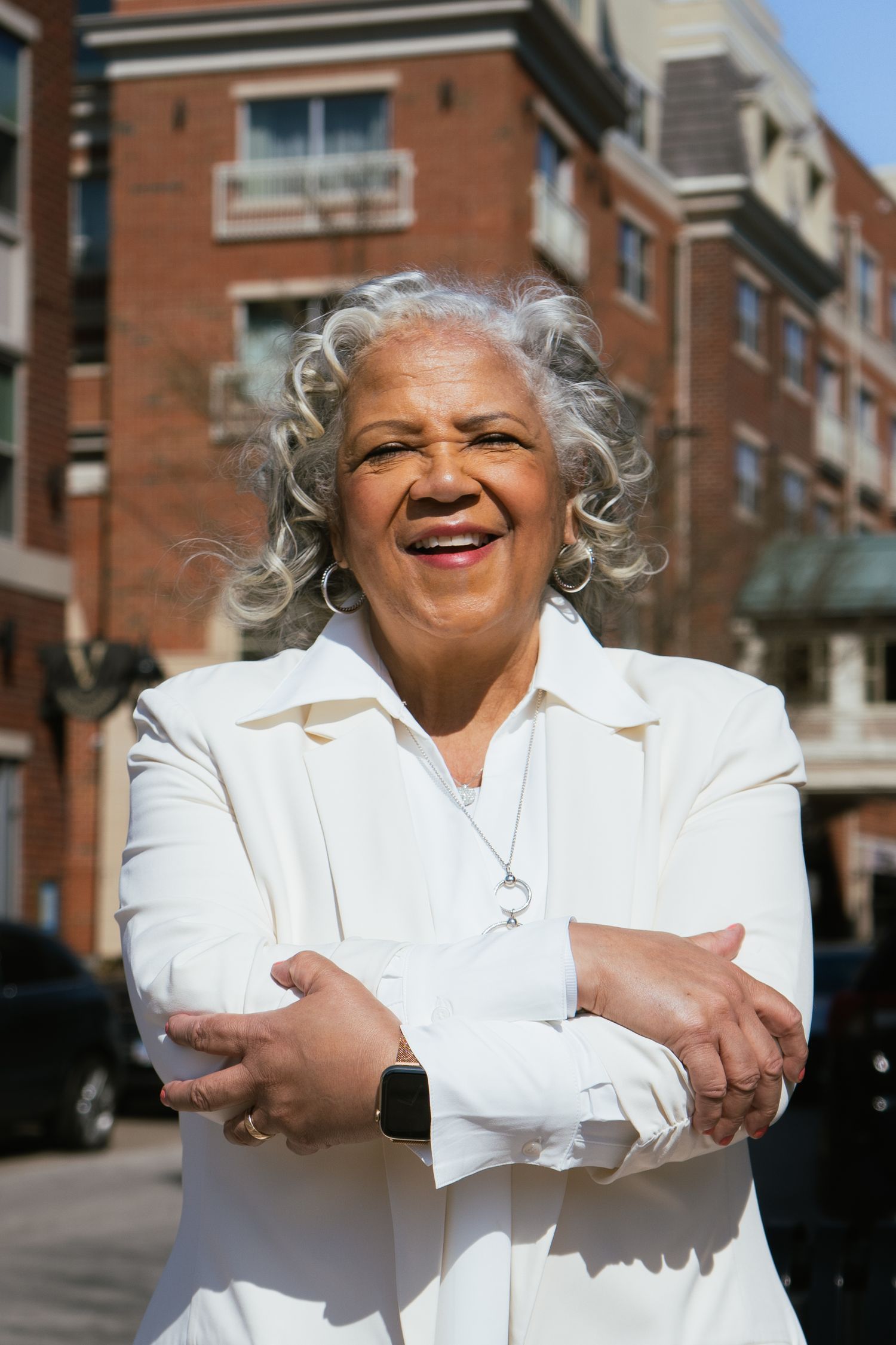 Four sequential photos show a person in a white outfit with silver hair smiling and crossing their arms against a brick building.