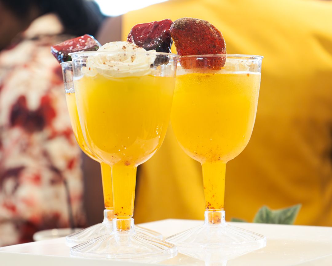 Yellow cocktails garnished with fresh fruit served in elegant stemmed glasses.