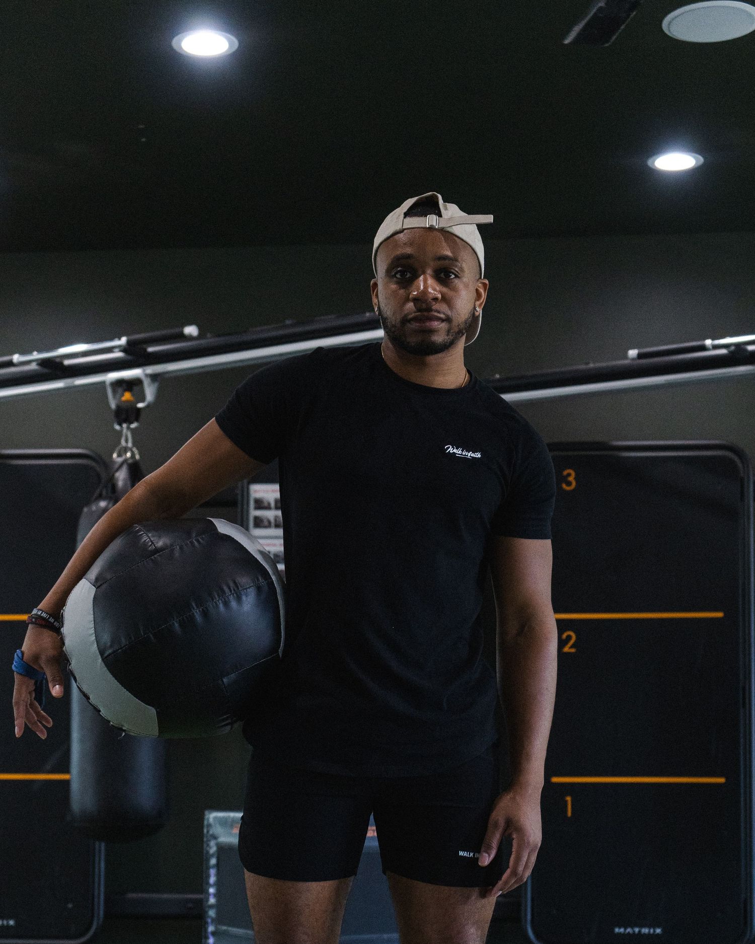 Athletic person in dark workout attire holding equipment in dimly lit gym setting.