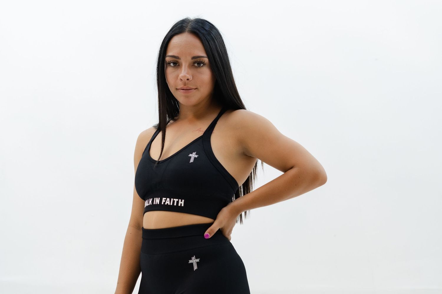 Woman in black athletic wear poses against white background during fitness photoshoot.