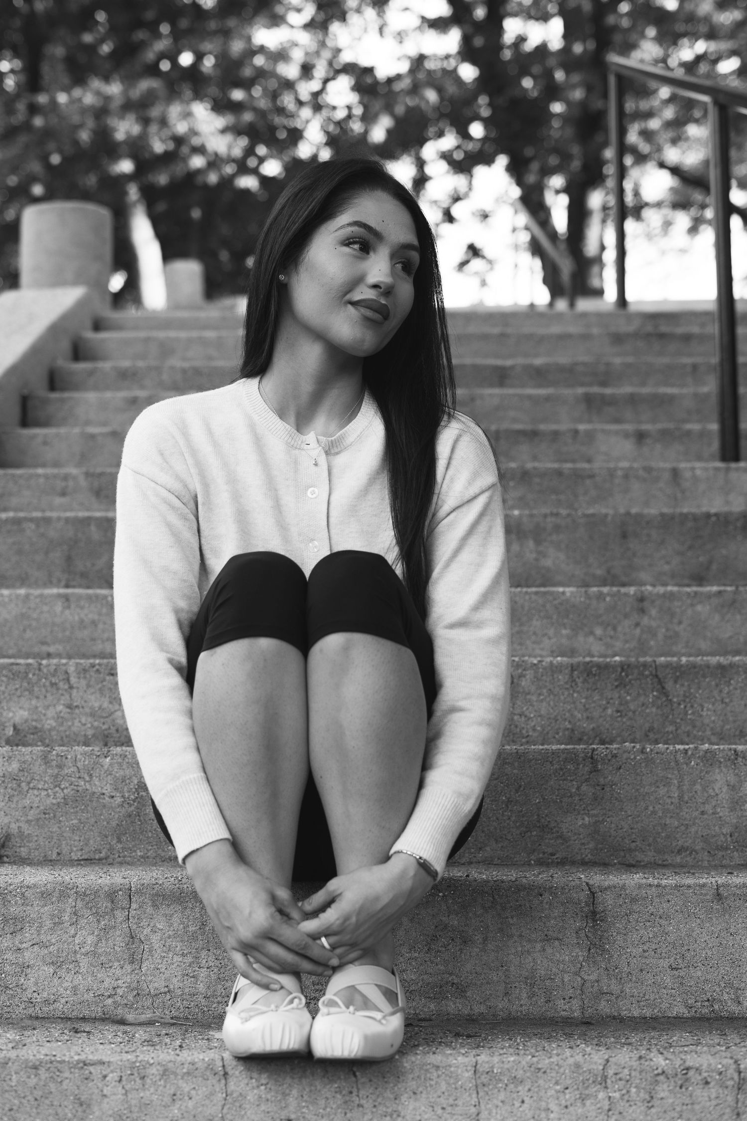 Young woman sitting on outdoor stone steps, hugging her knees, in black and white photography.