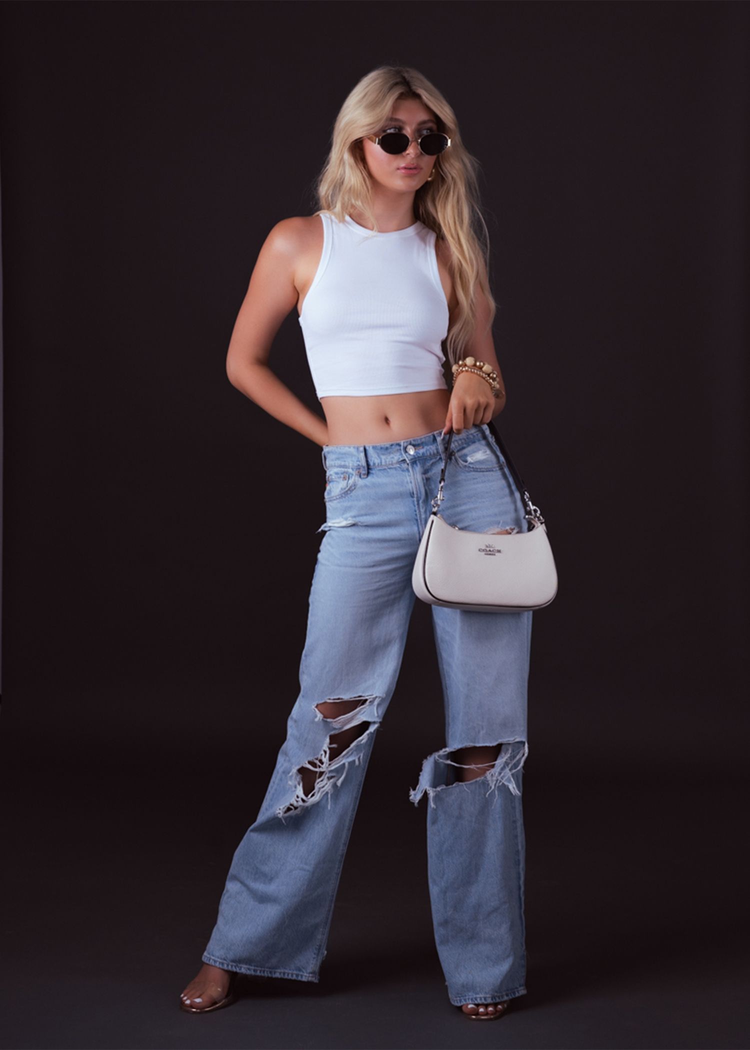 Studio fashion shoot with distressed wide-leg jeans and white crop top against black background.