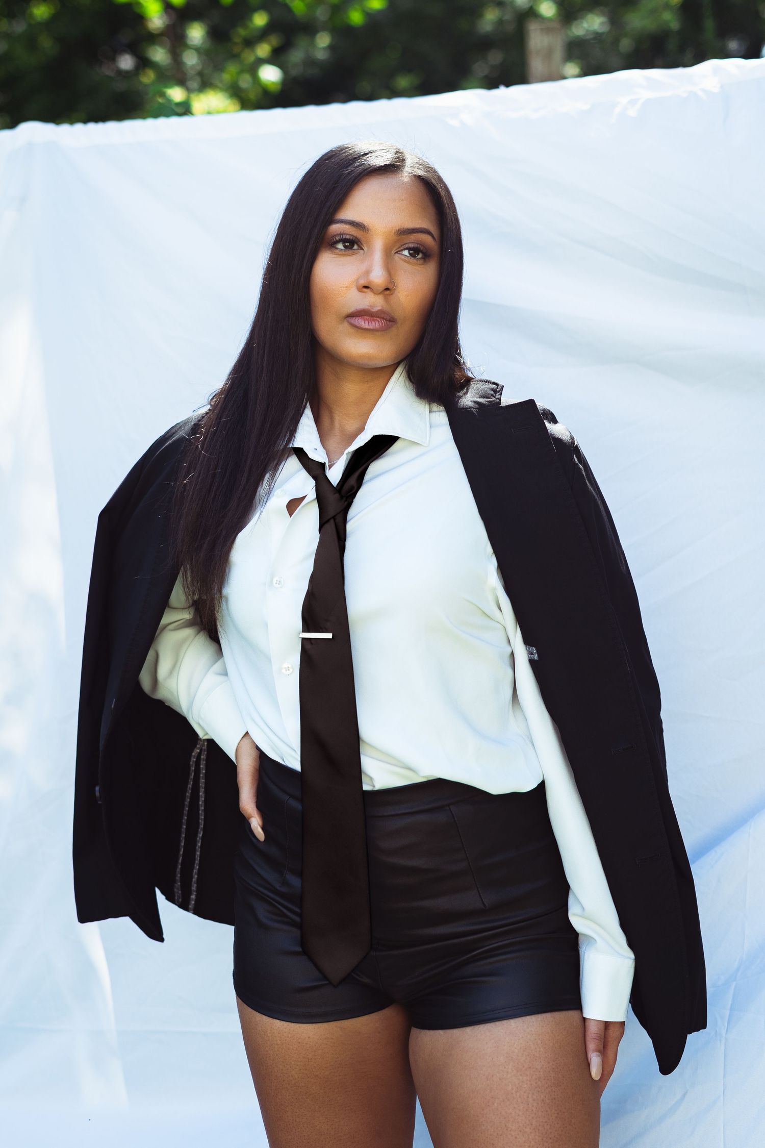 Fashion editorial model wearing black blazer and tie with white shirt in outdoor photoshoot.