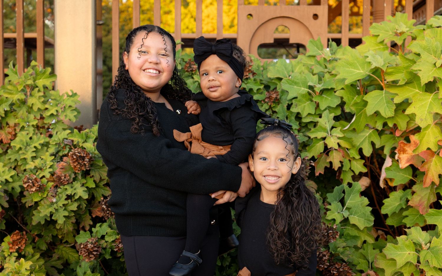 Outdoor family photoshoot with natural foliage and warm lighting in the background.