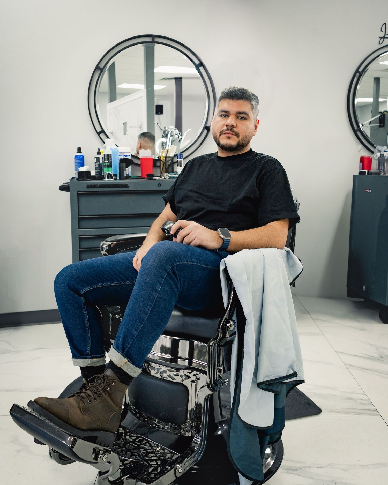 Person sitting in a barber chair wearing jeans and a black t-shirt in a modern salon setting.