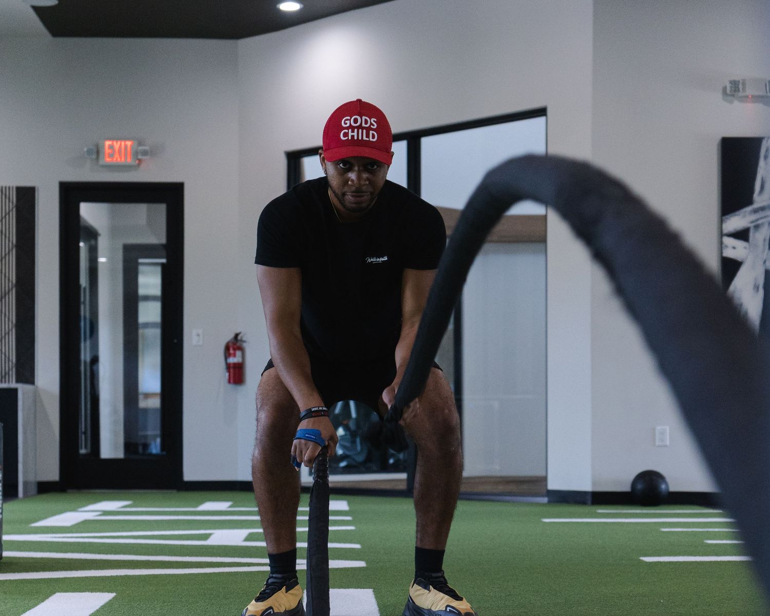 Athletic figure in black attire and red cap performing a workout routine in a modern gym space.