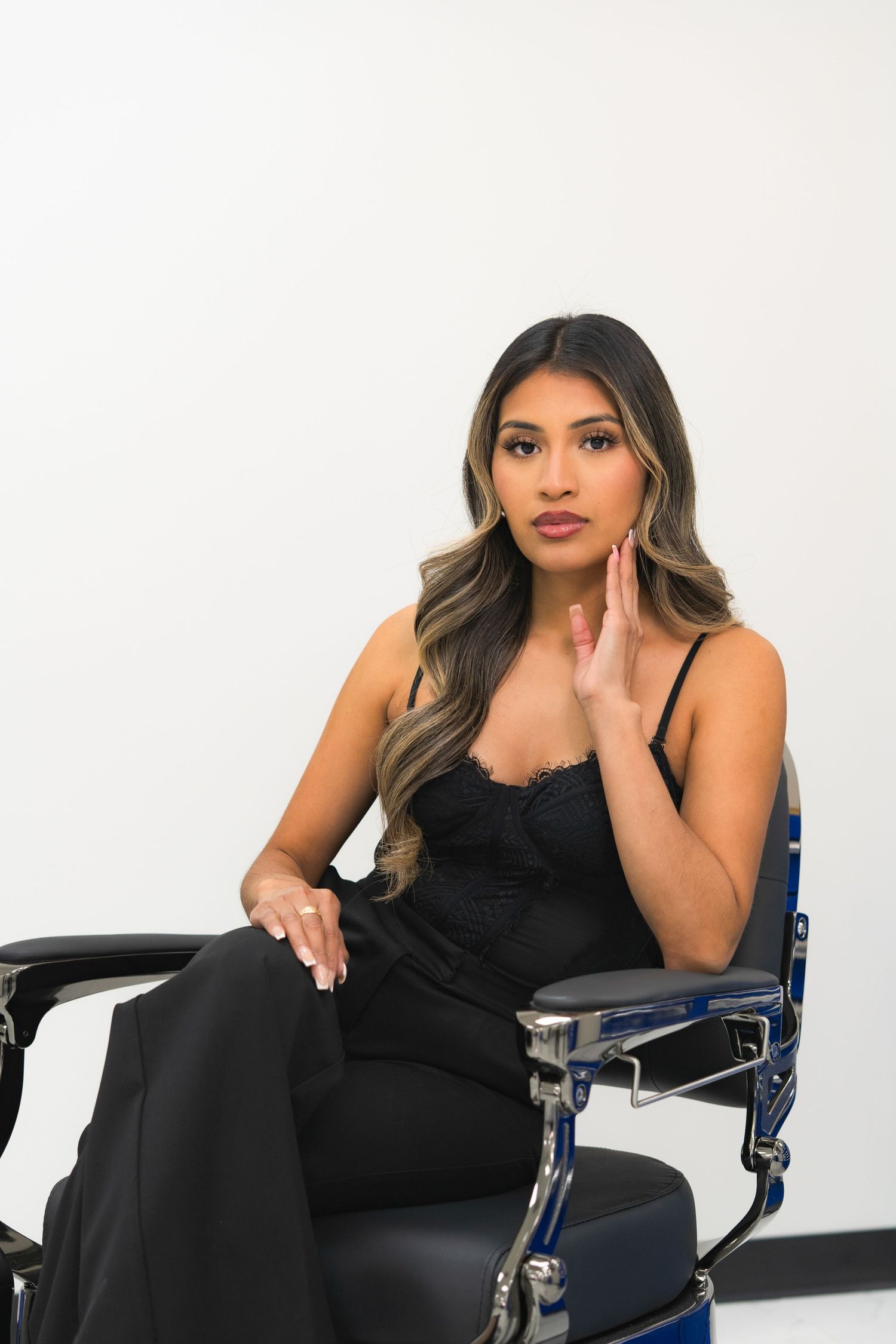 Woman in black dress poses elegantly on blue chair against white background in professional photo series.