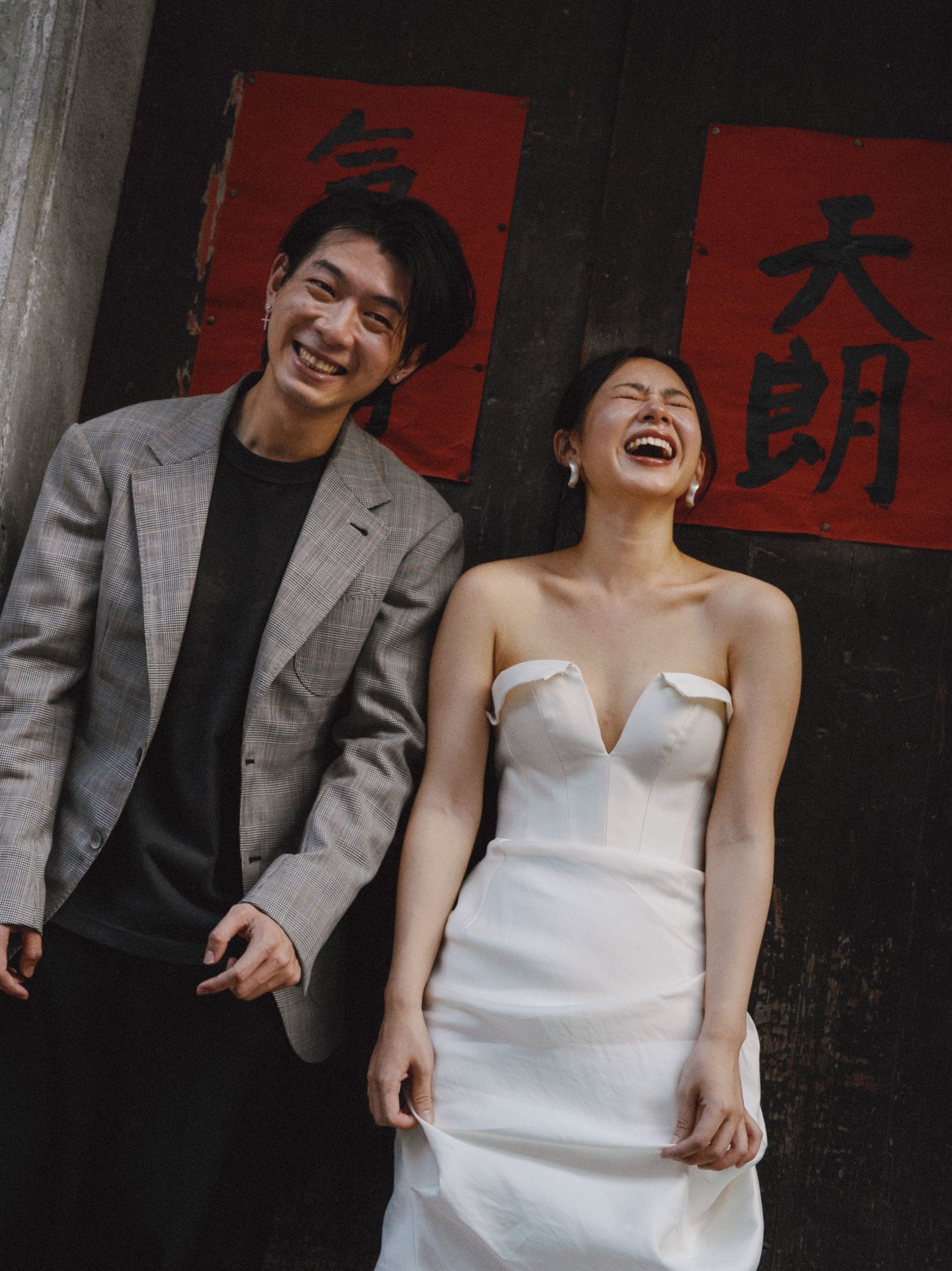 Asian couple laughing together in front of traditional red banners in a film-inspired style; San Francisco Bay Area; Mandarin, Cantonese,
