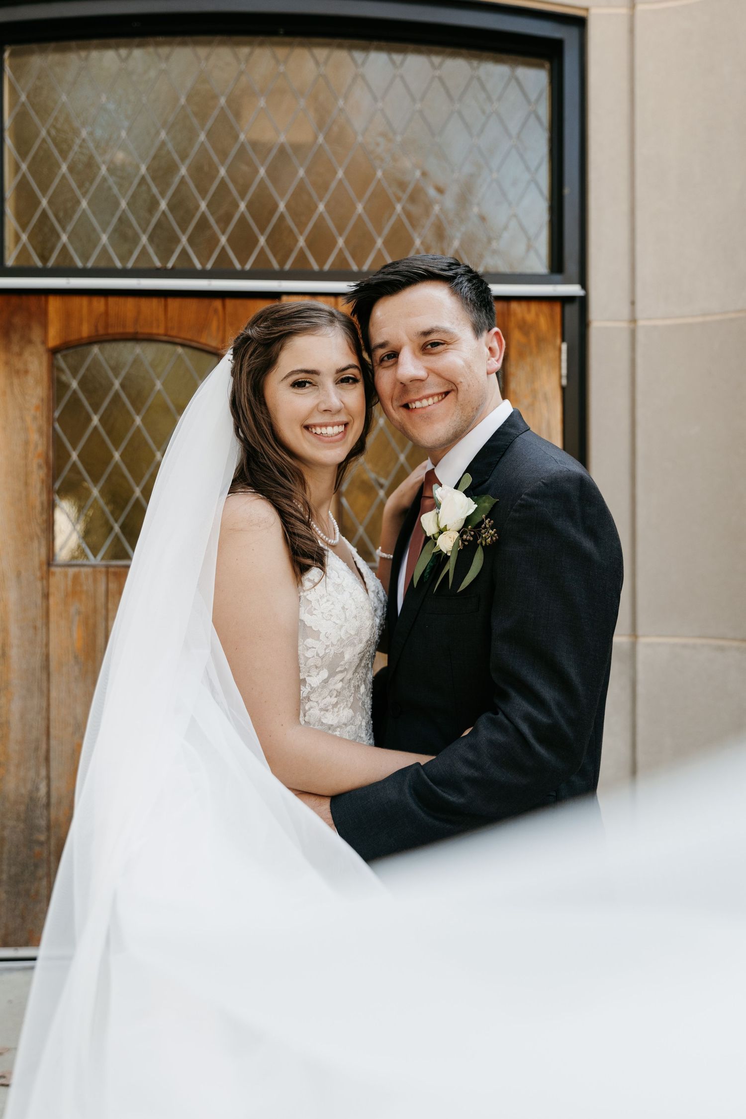Wedding portrait in front of brick building with decorative glass windows.