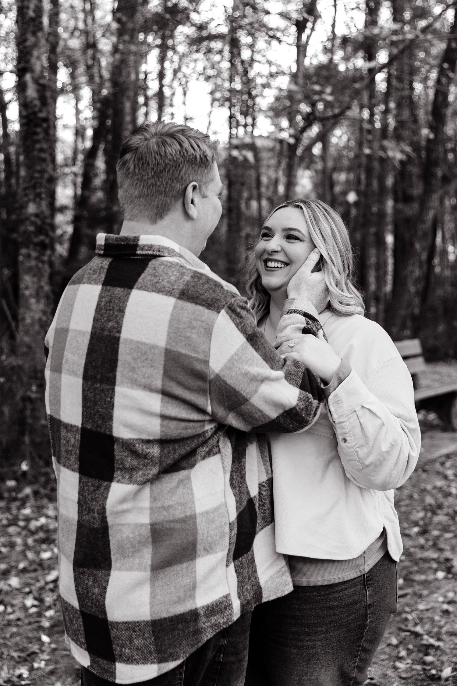 Black and white photo of a couple laughing together in a forest setting.